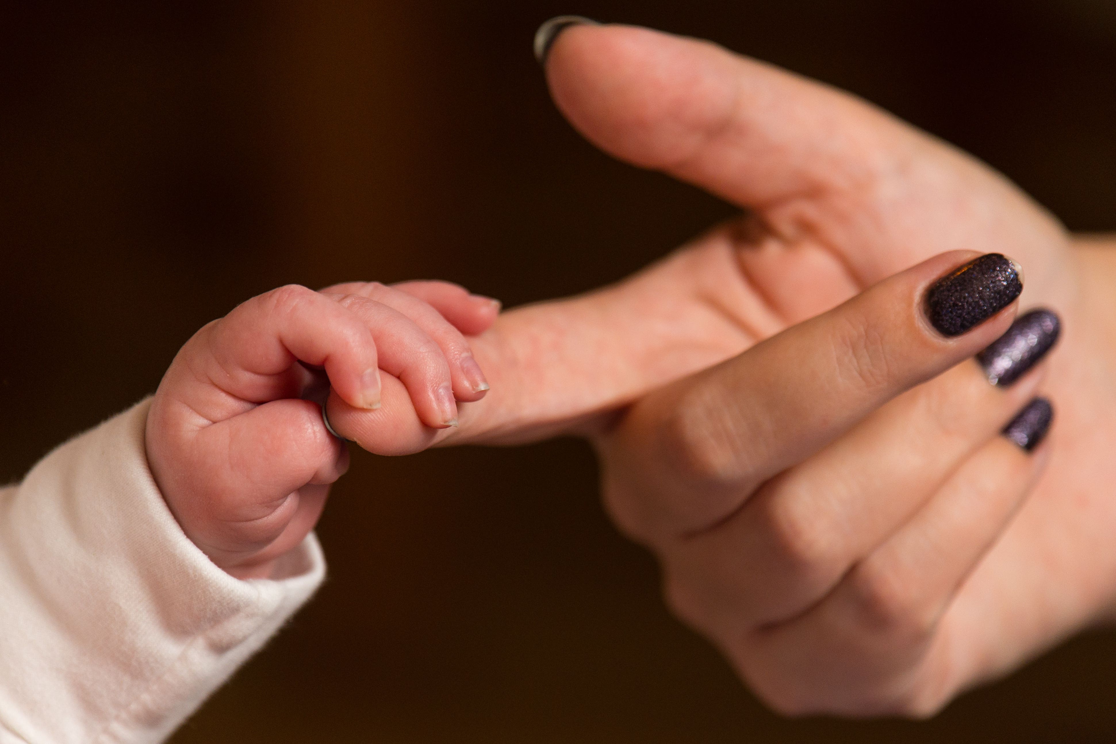 A baby boy, possibly Boy, grabs the finger of his mother