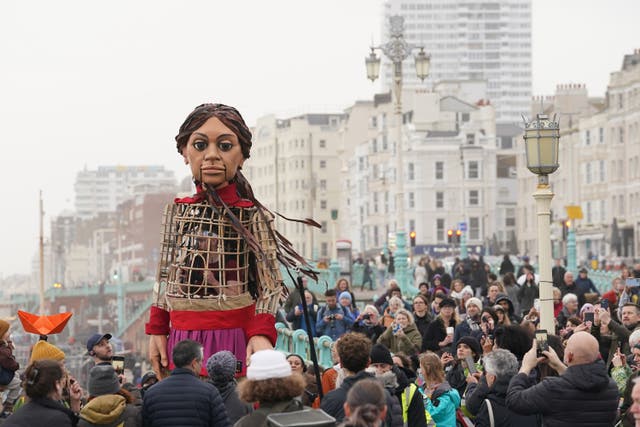 The Little Amal giant puppet of a 10-year-old Syrian refugee girl leads an early evening walk along Brighton beach (Gareth Fuller/PA)