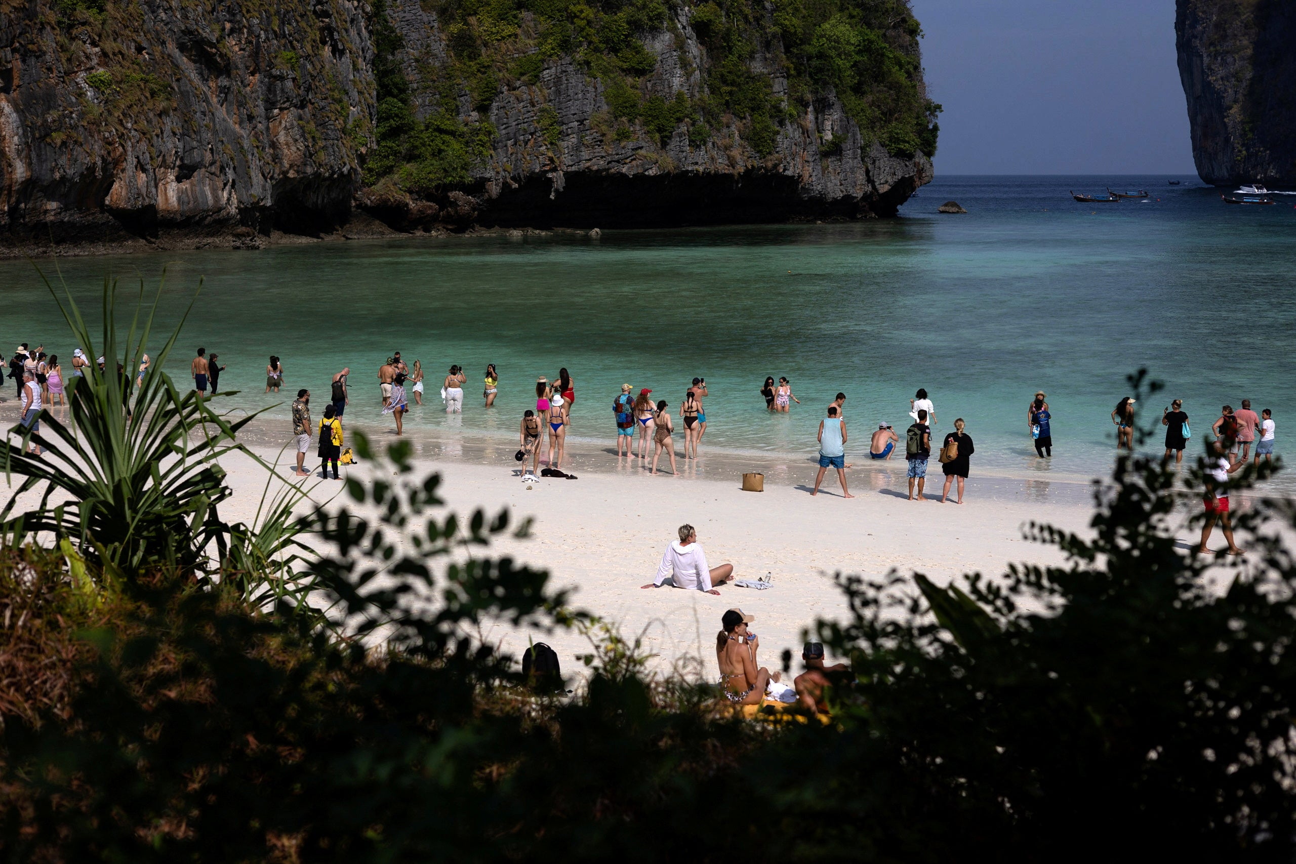 Tourists enjoy the beach where swimming is forbidden and people are only allowed to enter water up to their knees