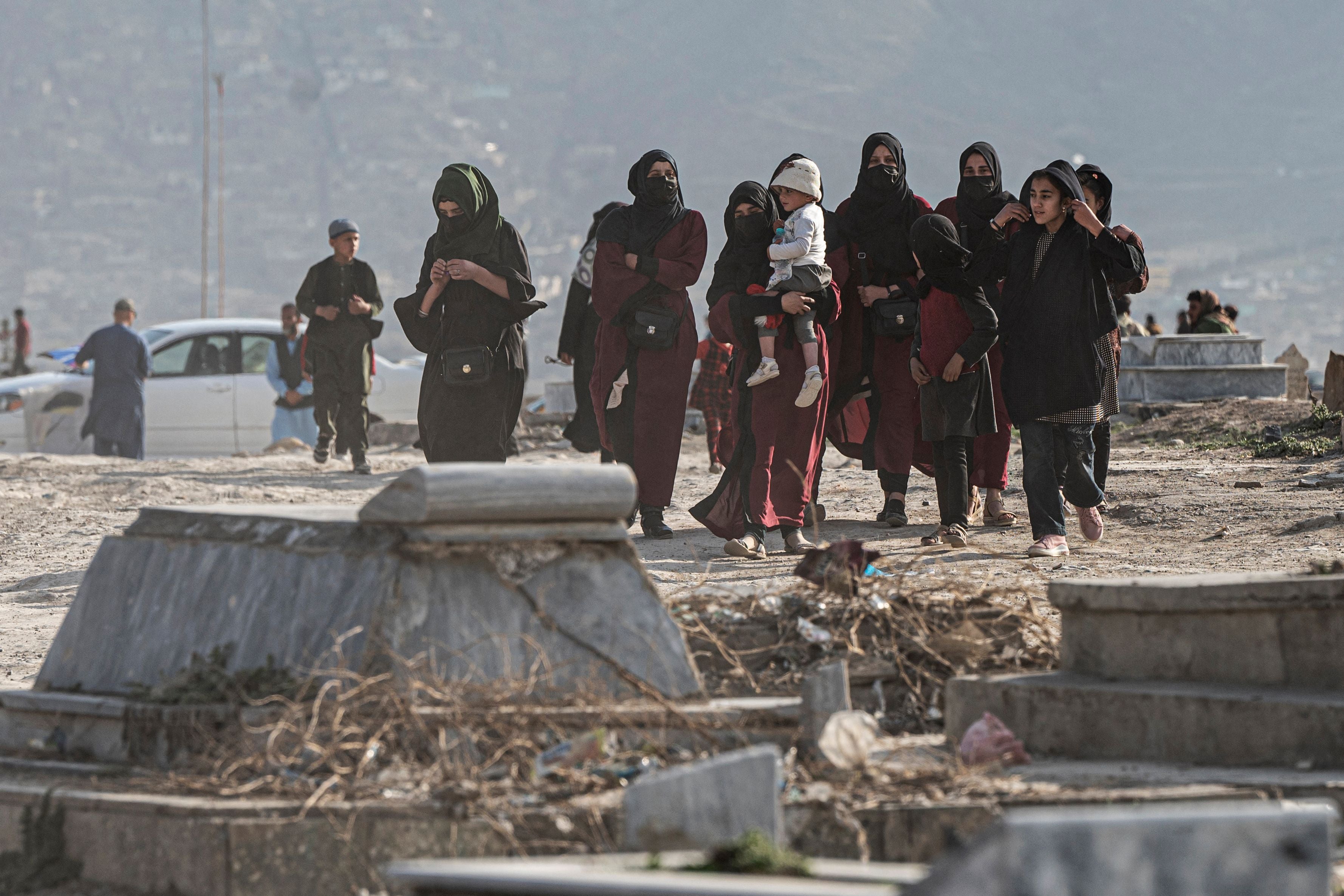 Afghan women with children walk at a graveyard at a hilltop in Kabul, Afghanistan