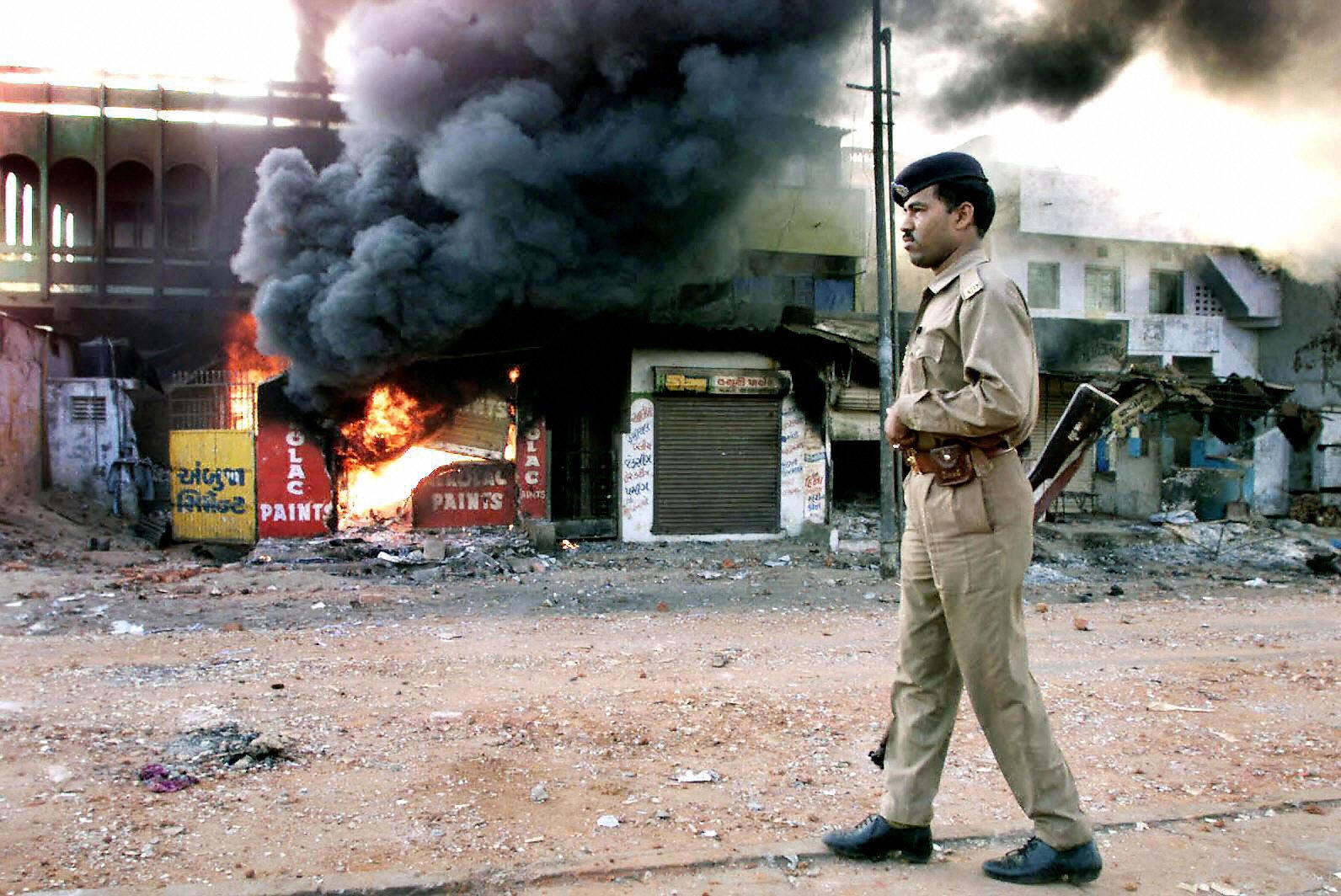 In this picture taken on 1 March 2002, an Indian policeman looks on as a row of shops burn during the Gujarat riots
