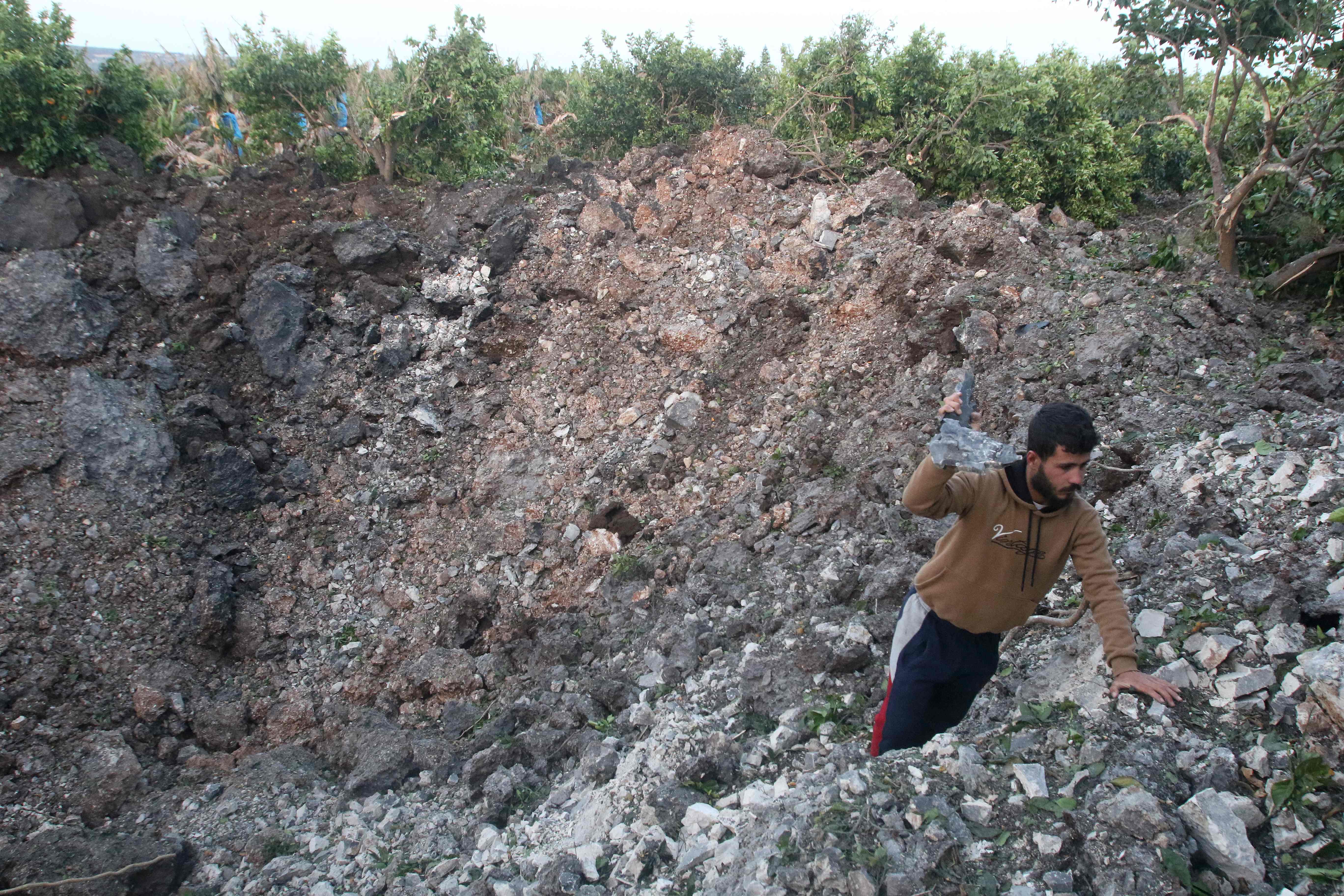 A man holds shrapnel in a crater left by a rocket following Israeli air strikes in Al Qulaylah