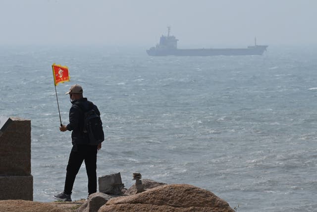 <p>A man walks with a flag as a ship passes by behind him on Pingtan island, the closest point to Taiwan, in Chinas southeast Fujian province on 8 April</p>