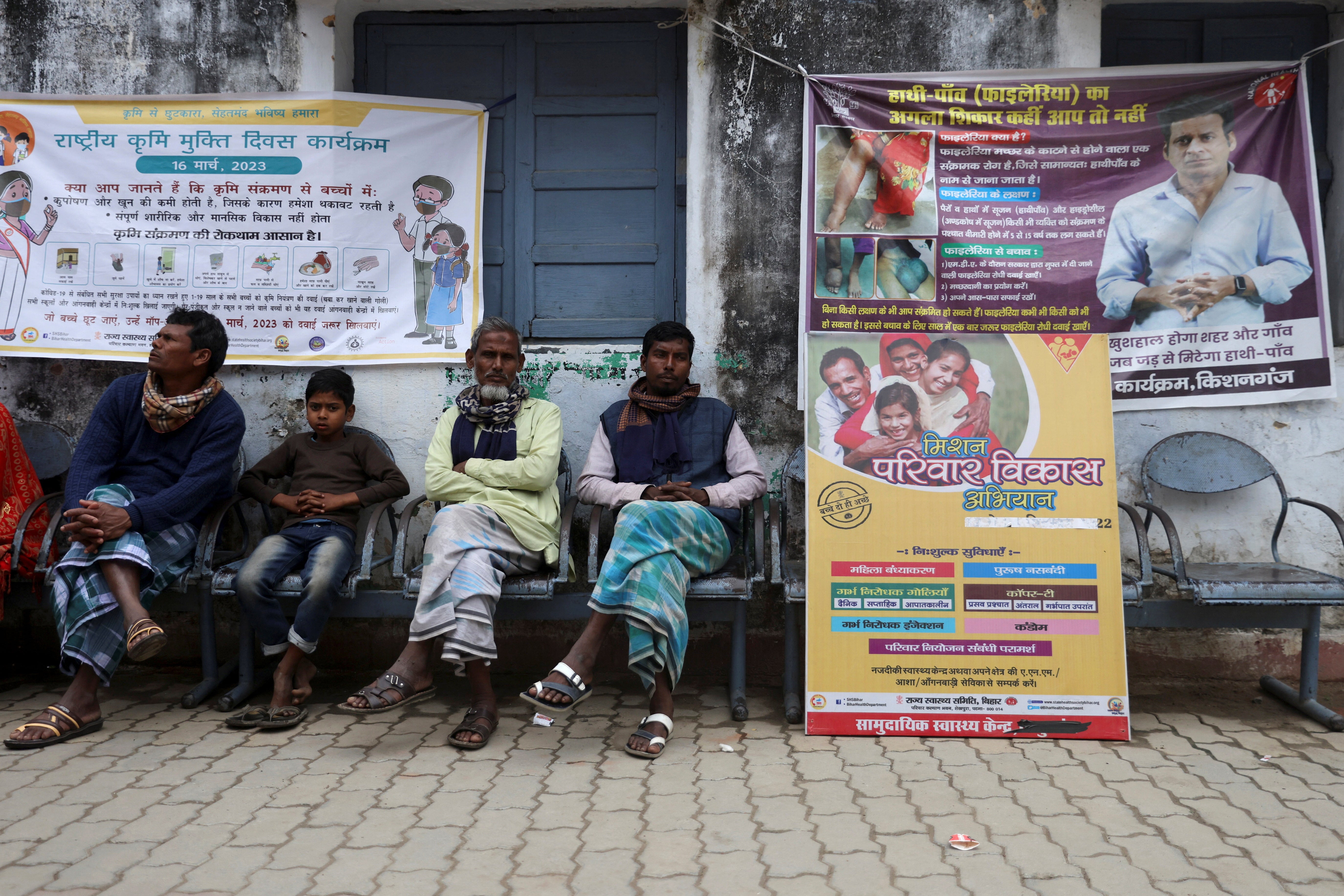 Men sit next to a board in Belwa village displaying information about the different family planning methods available