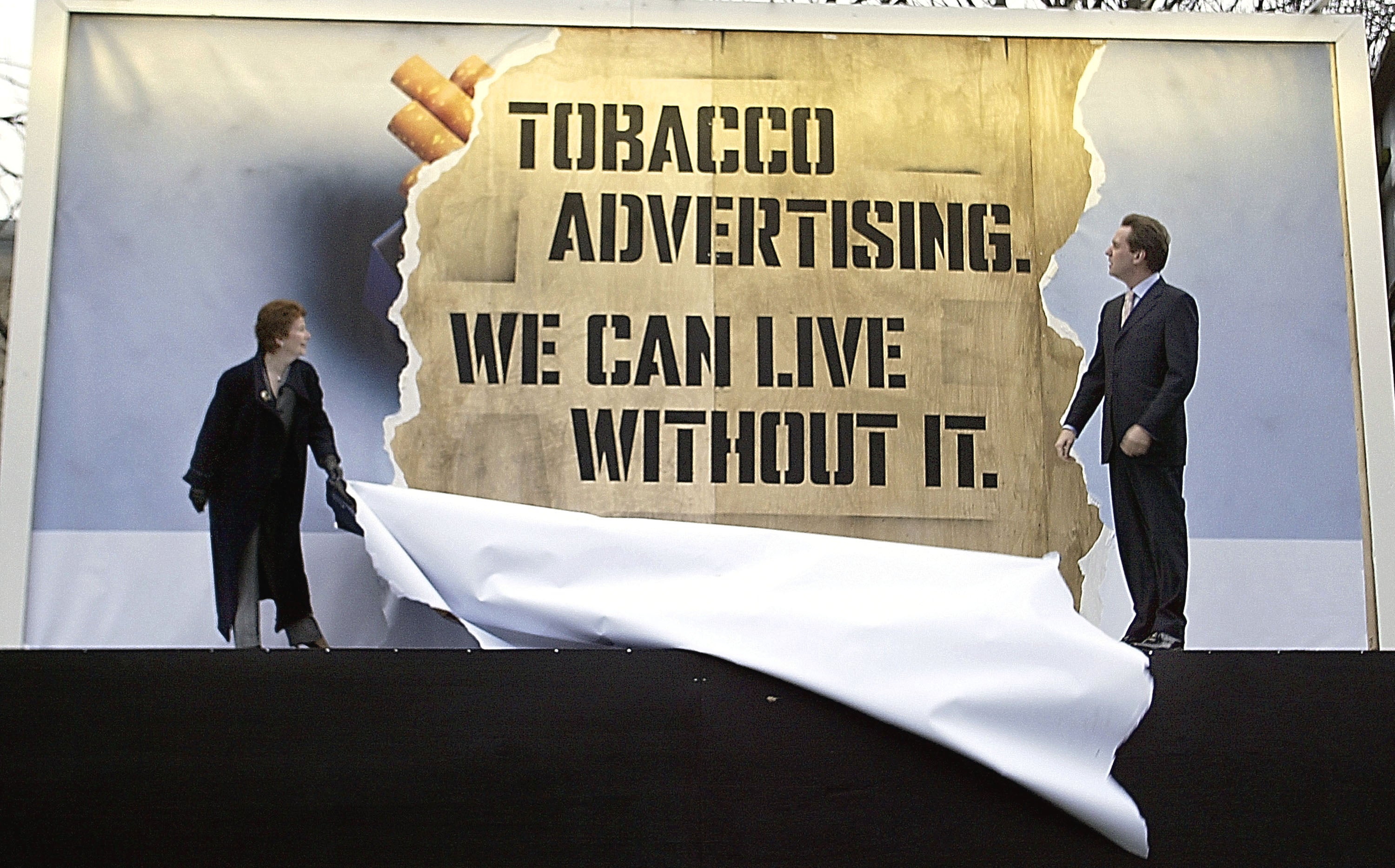 Milburn and health minister Hazel Blears tear down a tobacco billboard to reveal the message, 2003