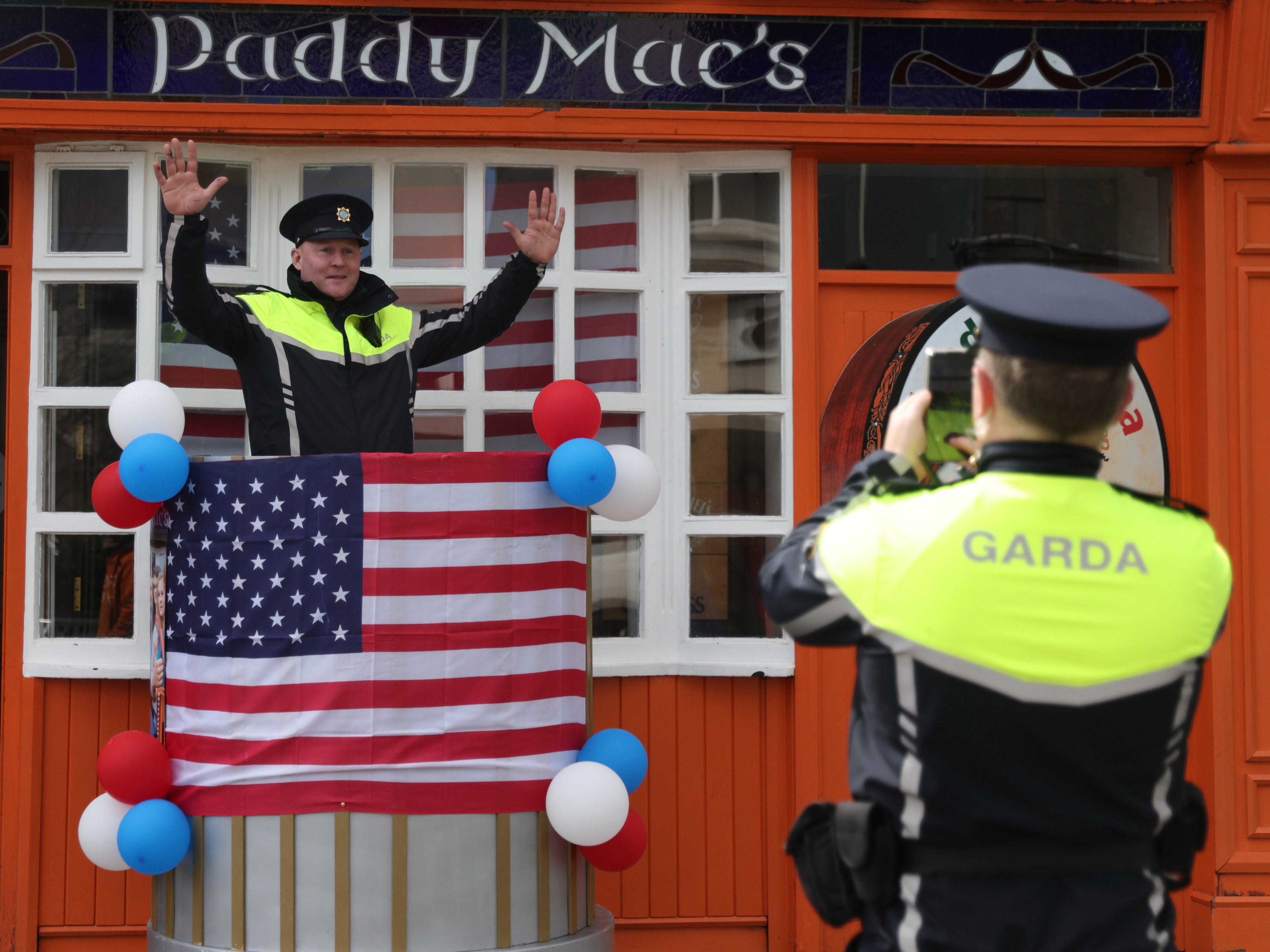 An Irish police officer poses for a colleague to take a photo as last minute preparation are made with bunting and US flags put up in Ballina