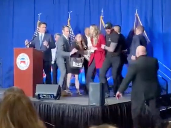 A pair of protesters from IfNotNow are led off-stage by security at a Republican fundraiser event in New Hampshire as Florida Governor Ron DeSantis watches from the podium