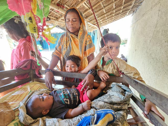 <p>Parveen Begum, who has had 11 children, tends to her latest child as her extended family huddles around her</p>