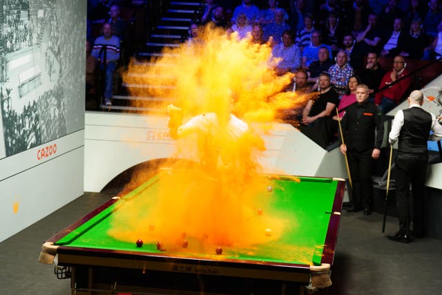 A Just Stop Oil protester jumps on the table and throws orange powder during the match between Robert Milkins against Joe Perry during day three of the Cazoo World Snooker Championship at the Crucible Theatre, Sheffield (Mike Egerton/PA)