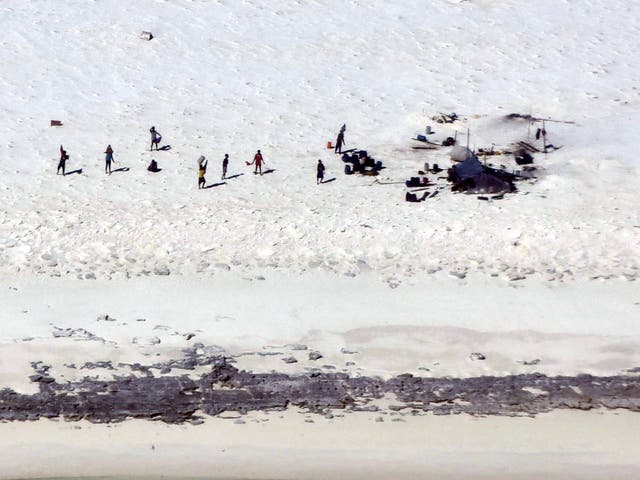 <p>Fishermen from Indonesia stand on a beach on Bedwell Island</p>