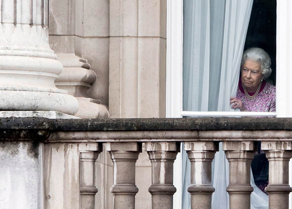 Queen Elizabeth II peers out a window from behind a curtain in Buckingham Palace