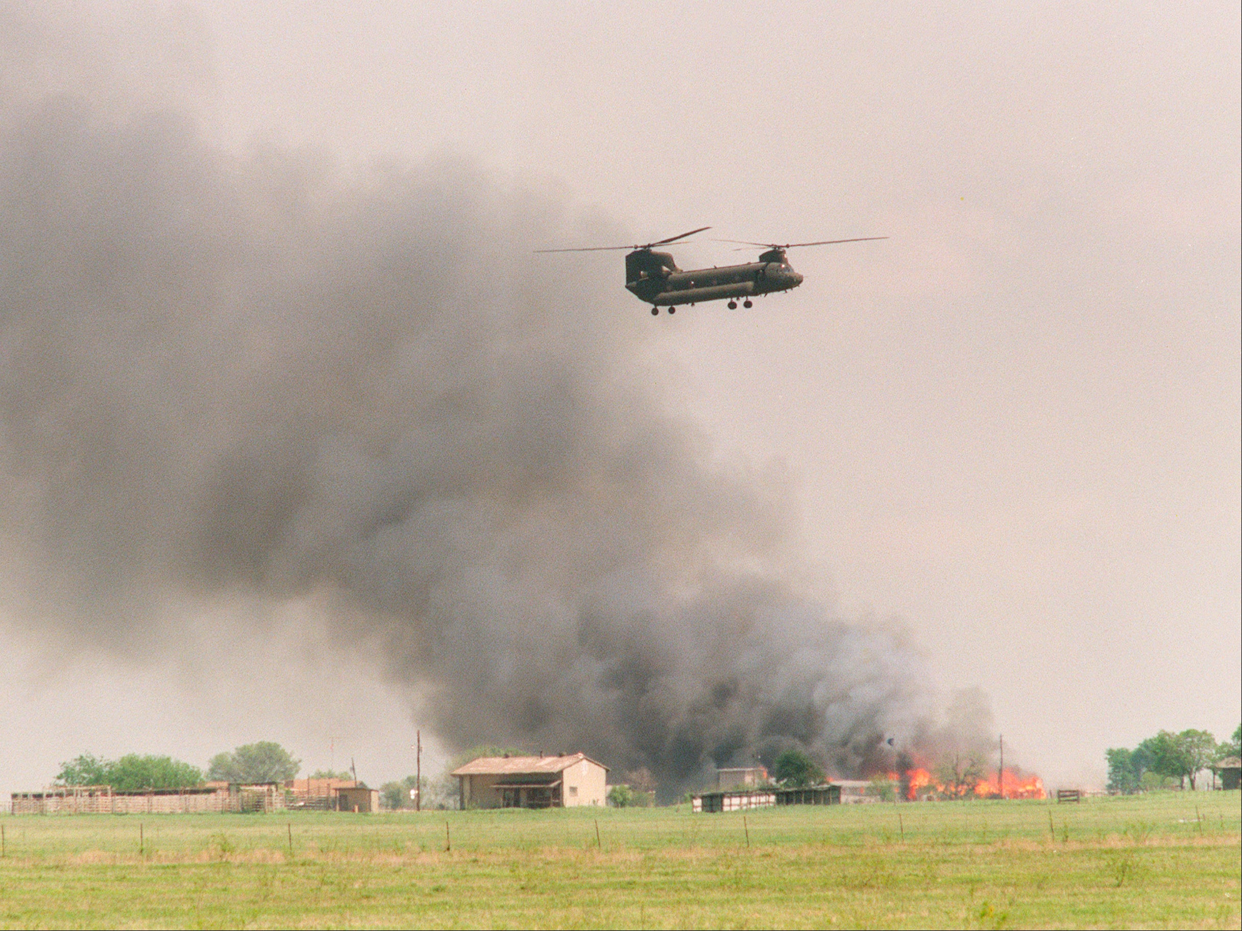 A National Guard helicopter flies past the burning Branch Davidian cult compound in Waco, Texas on 19 April 1993
