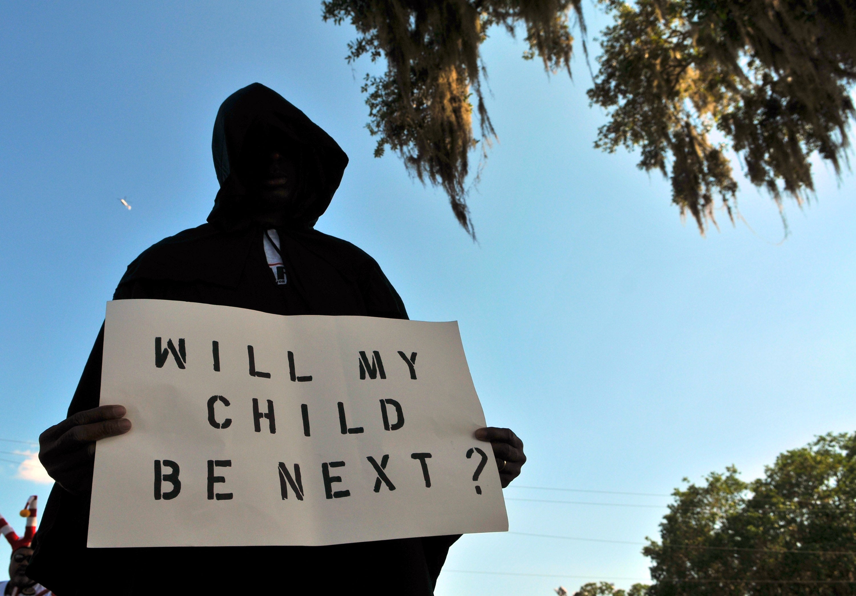 A man dressed in a hood holds up a sign saying "Will My Child Be Next?", during a protest march in Sanford, Florida following the 2012 killing of Trayvon Martin