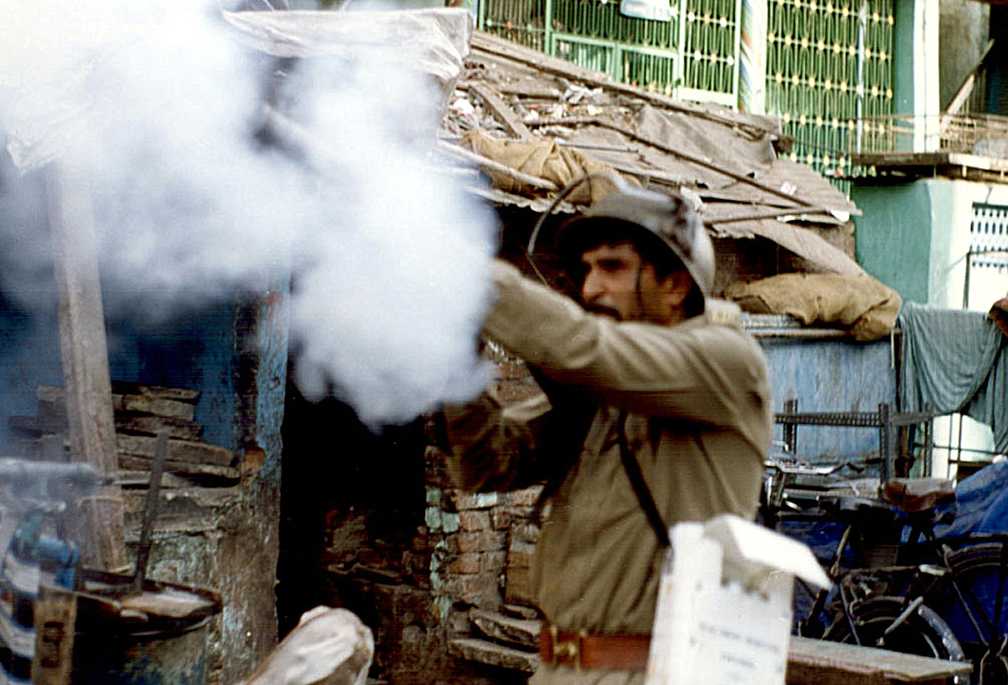 An Indian policeman shoot tear gas at rioters in Ahmedabad, 5 April 2002