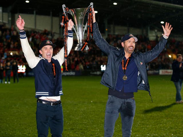 <p>Wrexham co-owners Rob McElhenney and Ryan Reynolds celebrate with the trophy on the pitch after Wrexham win the National League and promotion to League</p>