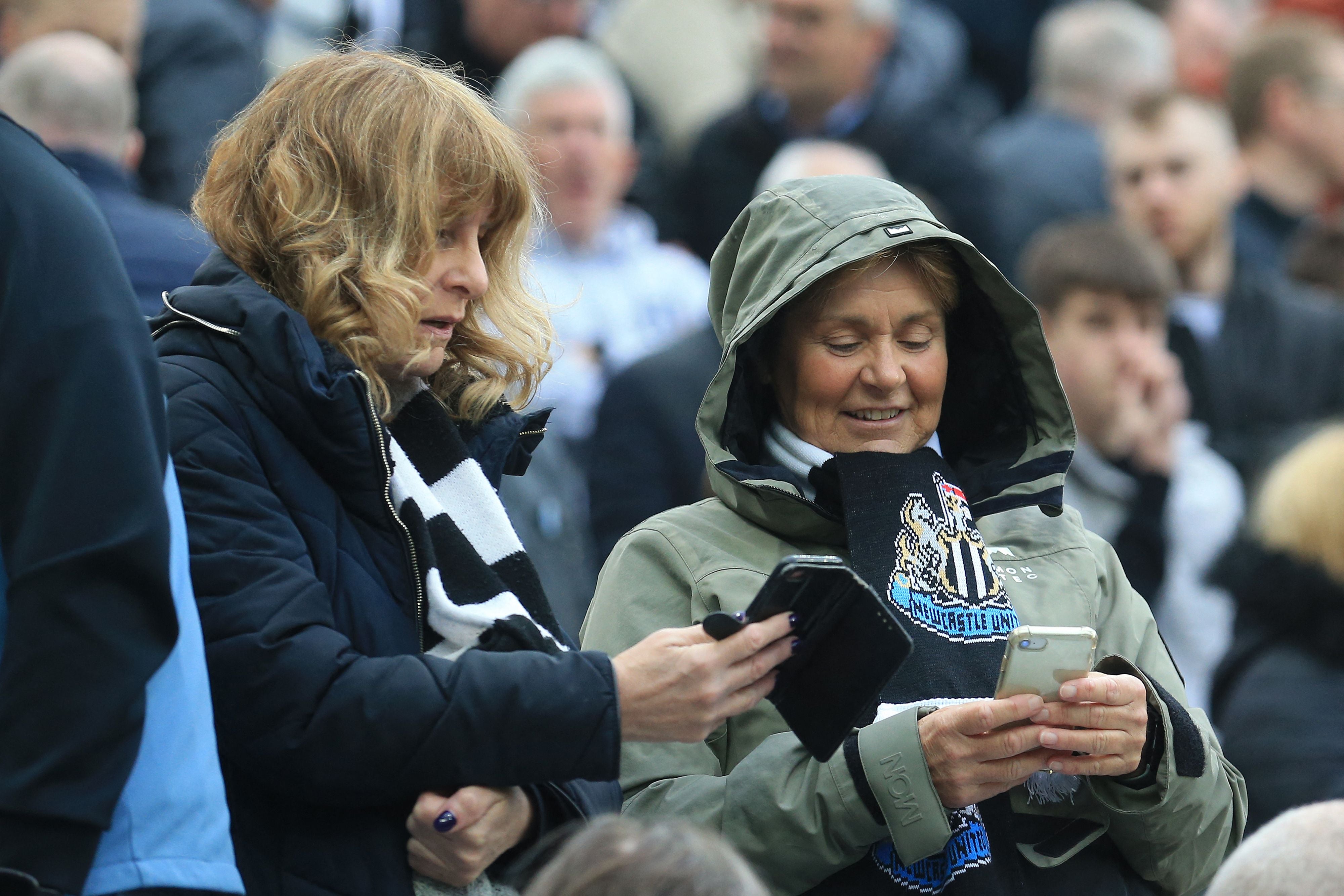 Fans check their phones as an 'Emergency Alert' is sent to smart phone owners in the UK, during the English Premier League football match between Newcastle United and Tottenham Hotspur at St James' Park in Newcastle