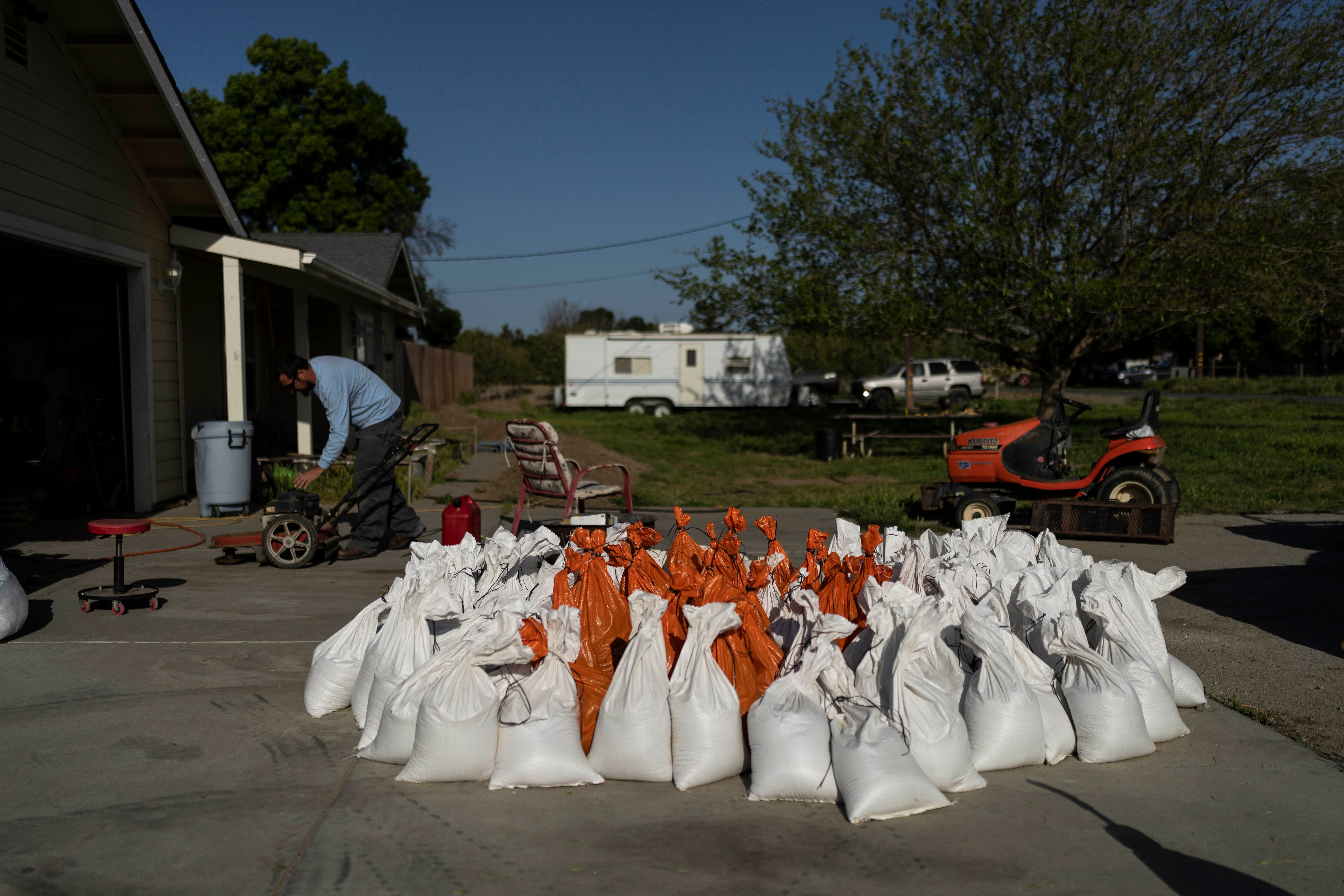 Brennon Williams operates a lawn mower at his girlfriend's home as sandbags are prepared in anticipation of flooding of the Kings River in the Island District of Lemoore