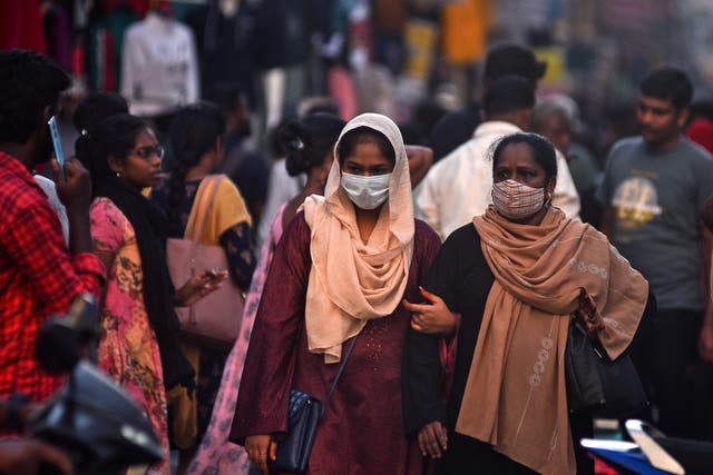 <p>Women wear masks as they pass through a crowded street, amidst the spike in Covid-19 cases</p>