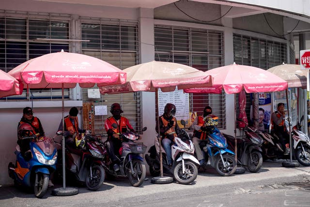 <p>Motorbike taxi drivers shelter from the sun under umbrellas during heatwave conditions in Bangkok, Thailand </p>
