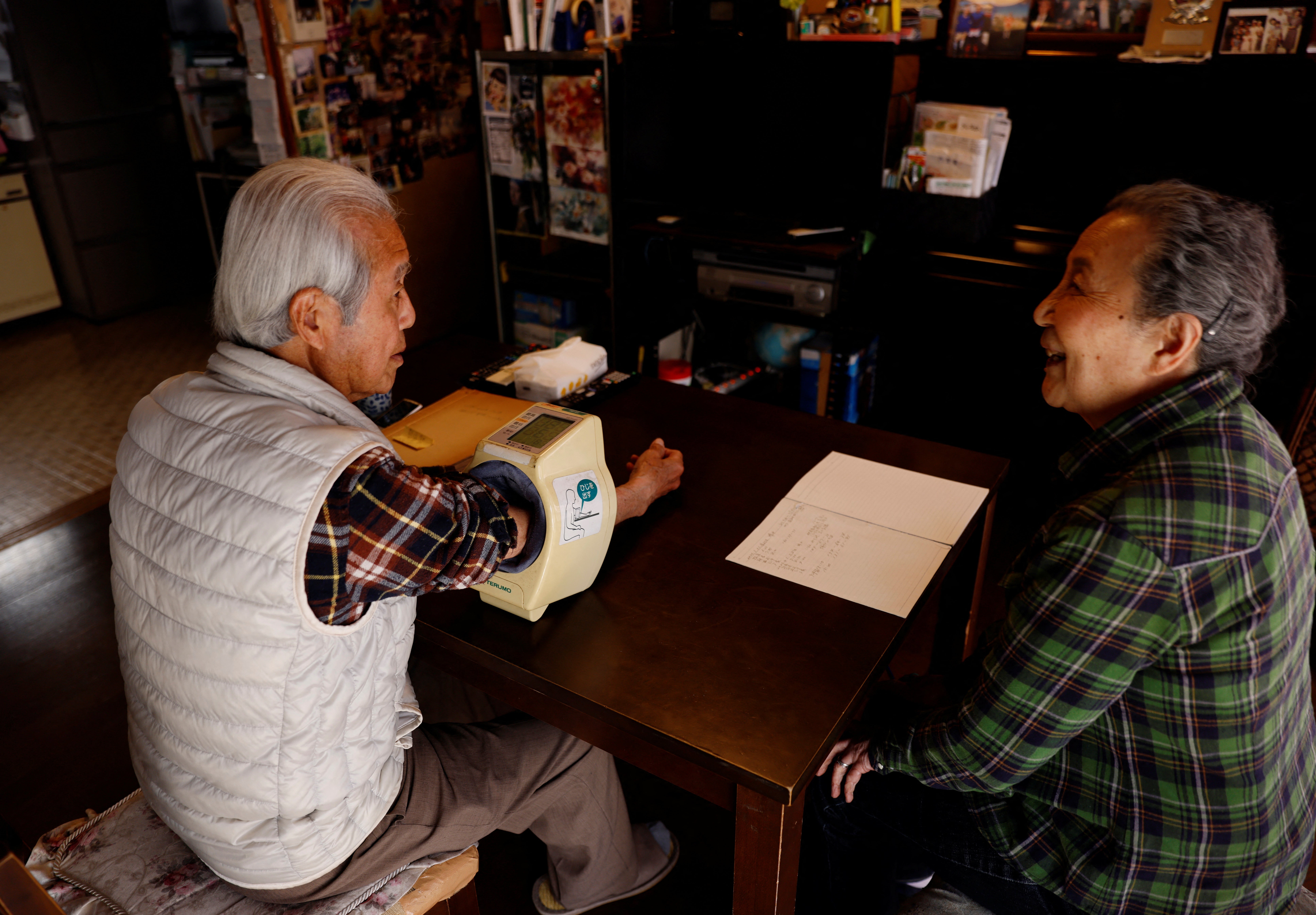 Nomura checks his blood pressure while his wife Junko Nomura, 80, writes down the reading on a notebook to keep record