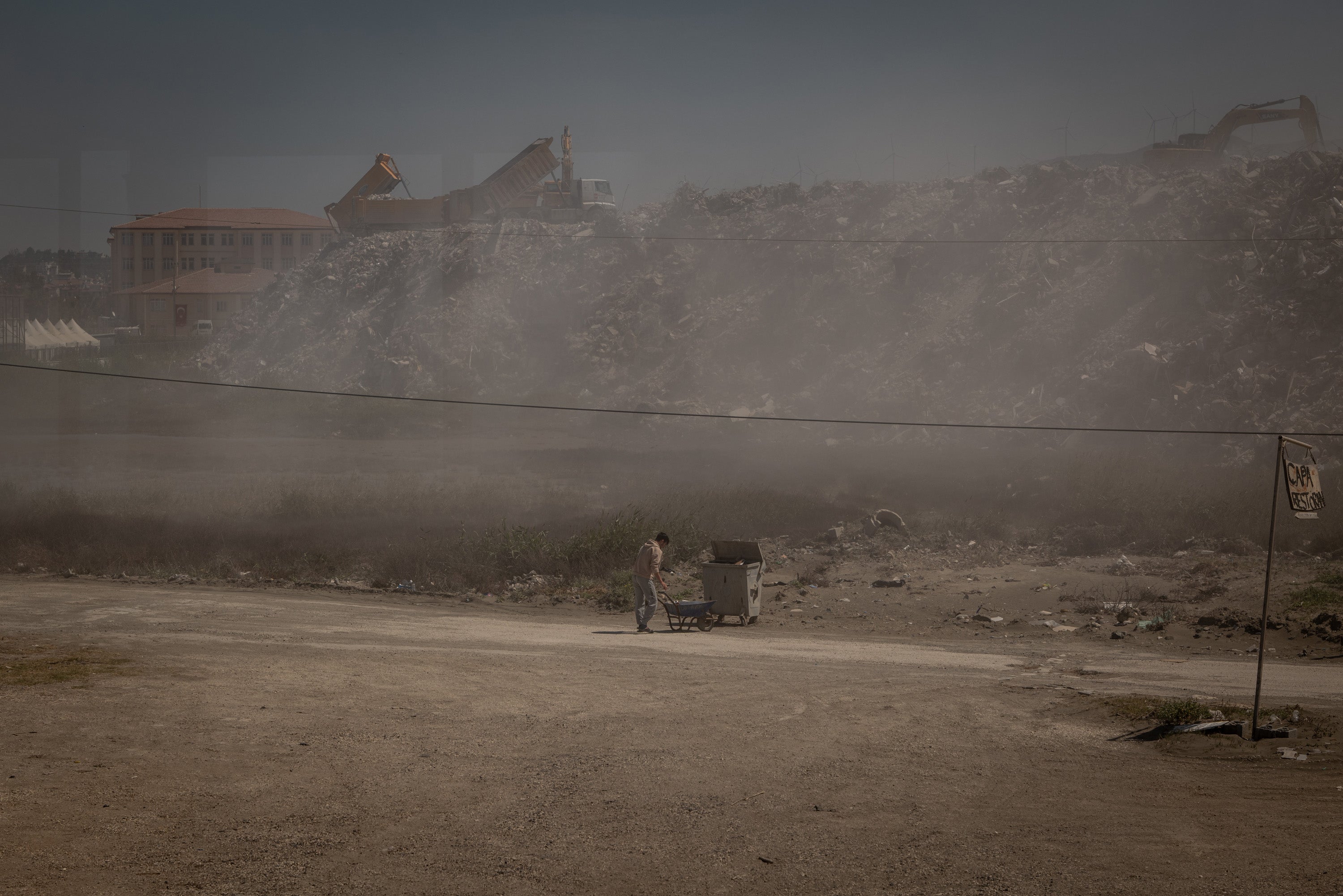 A restaurant worker disposes of trash amid a cloud of dust from rubble