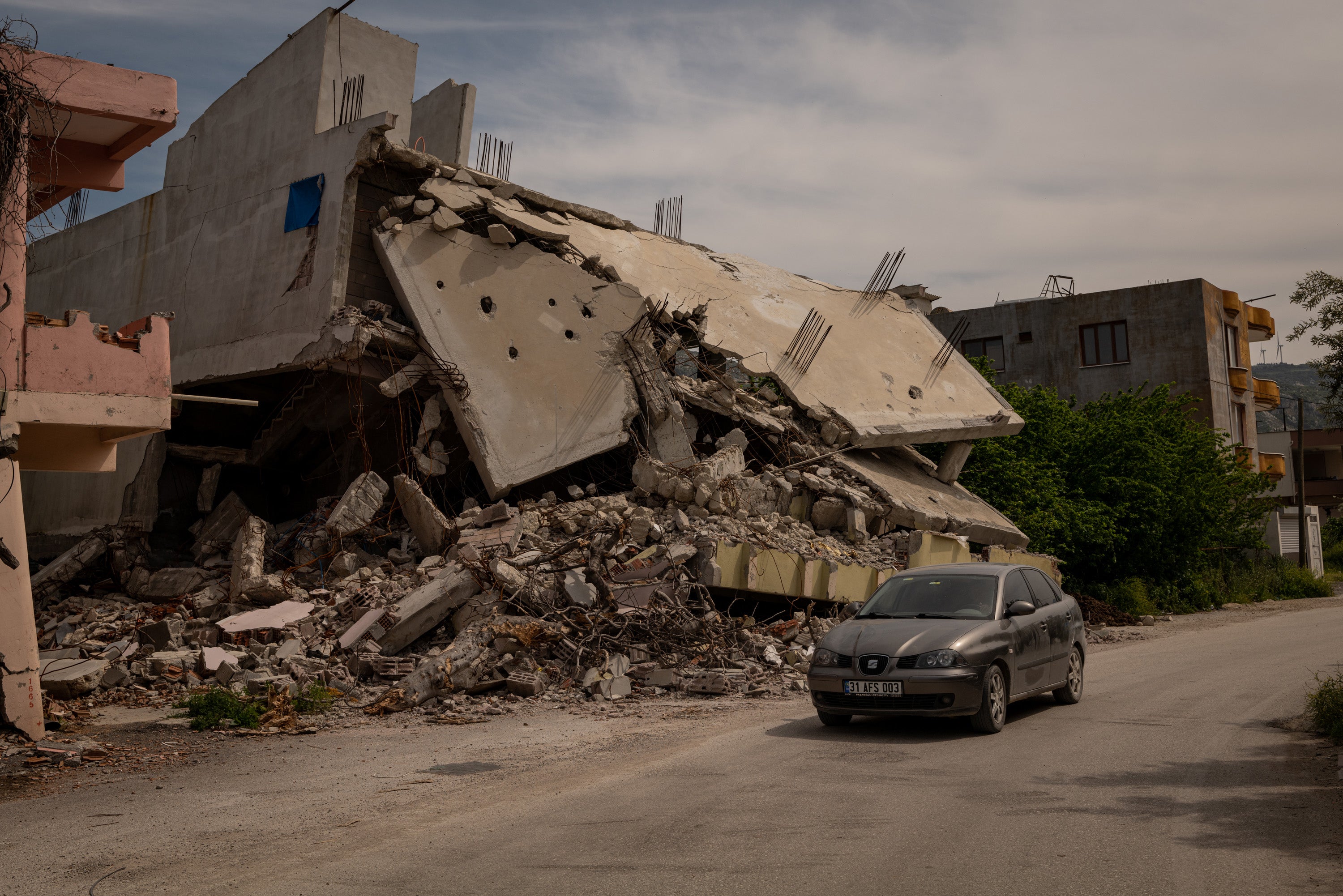 A car drives by a destroyed residential building in Samandag