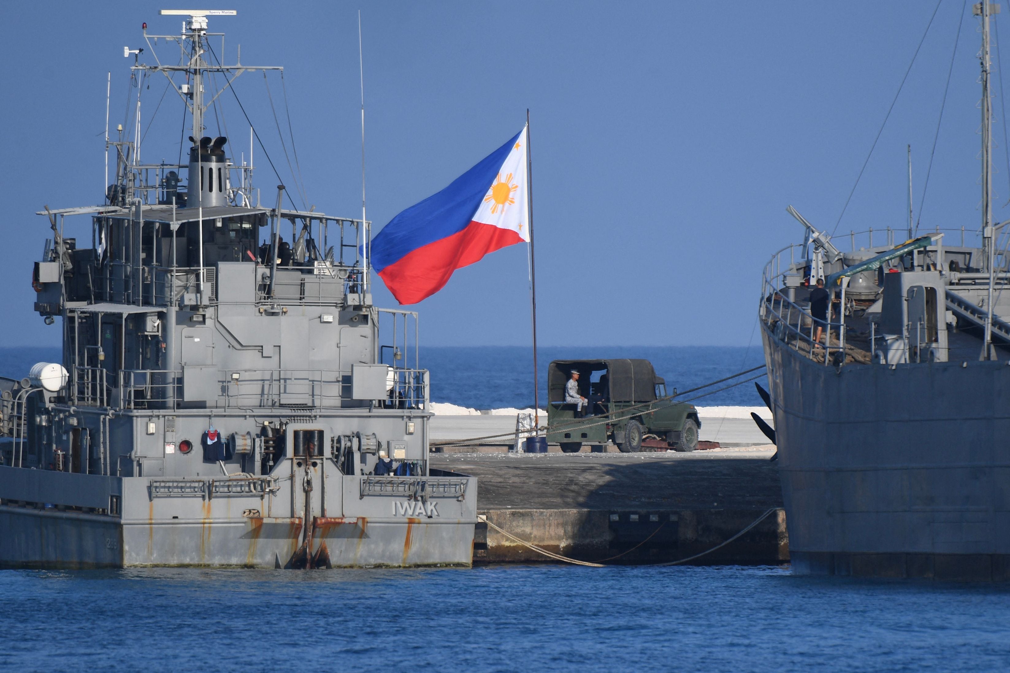 This photo taken on April 21, 2023 shows a Philippine flag fluttering next to navy ships anchored at the Philippine-occupied Thitu island in the disputed South China Sea