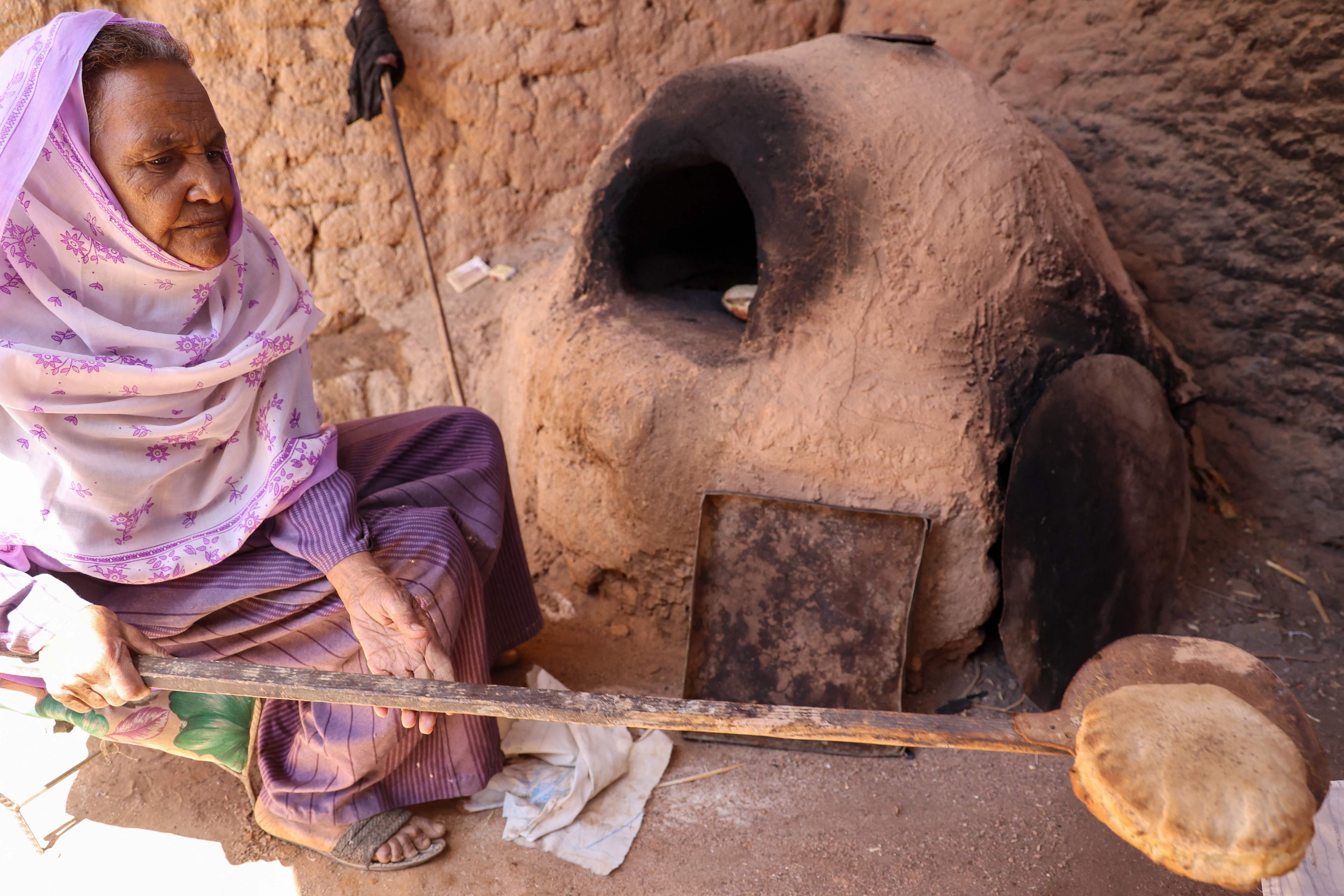 Local resident Naamat Jabal Sayyid Hasan, 75, bakes bread in a mud hut as she does daily to offer to people fleeing war-torn Sudan