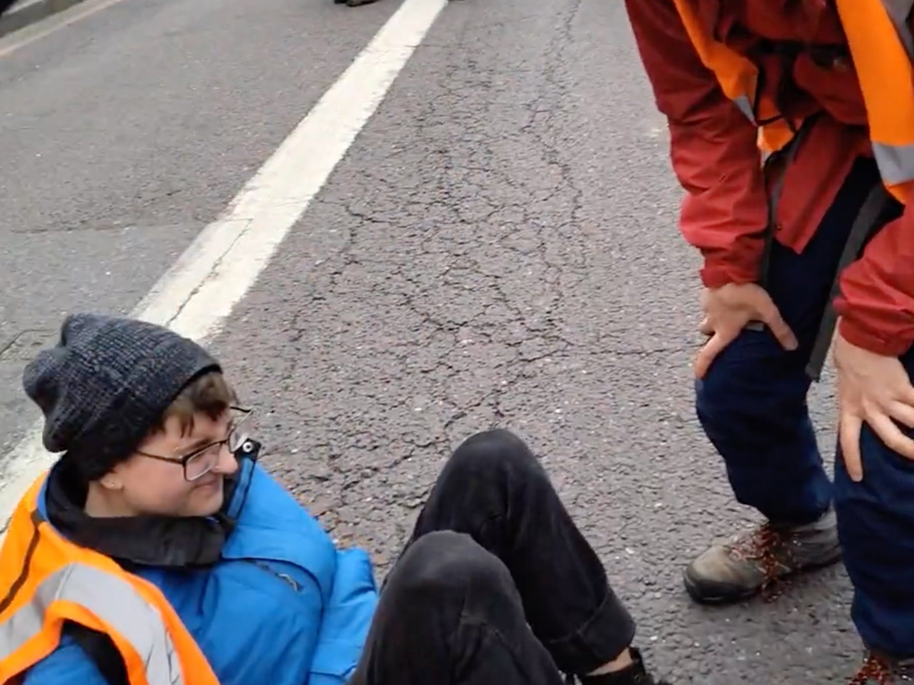 A protestor is seen sitting on the road following the collision, while activists around her claim the car “ran over her foot”
