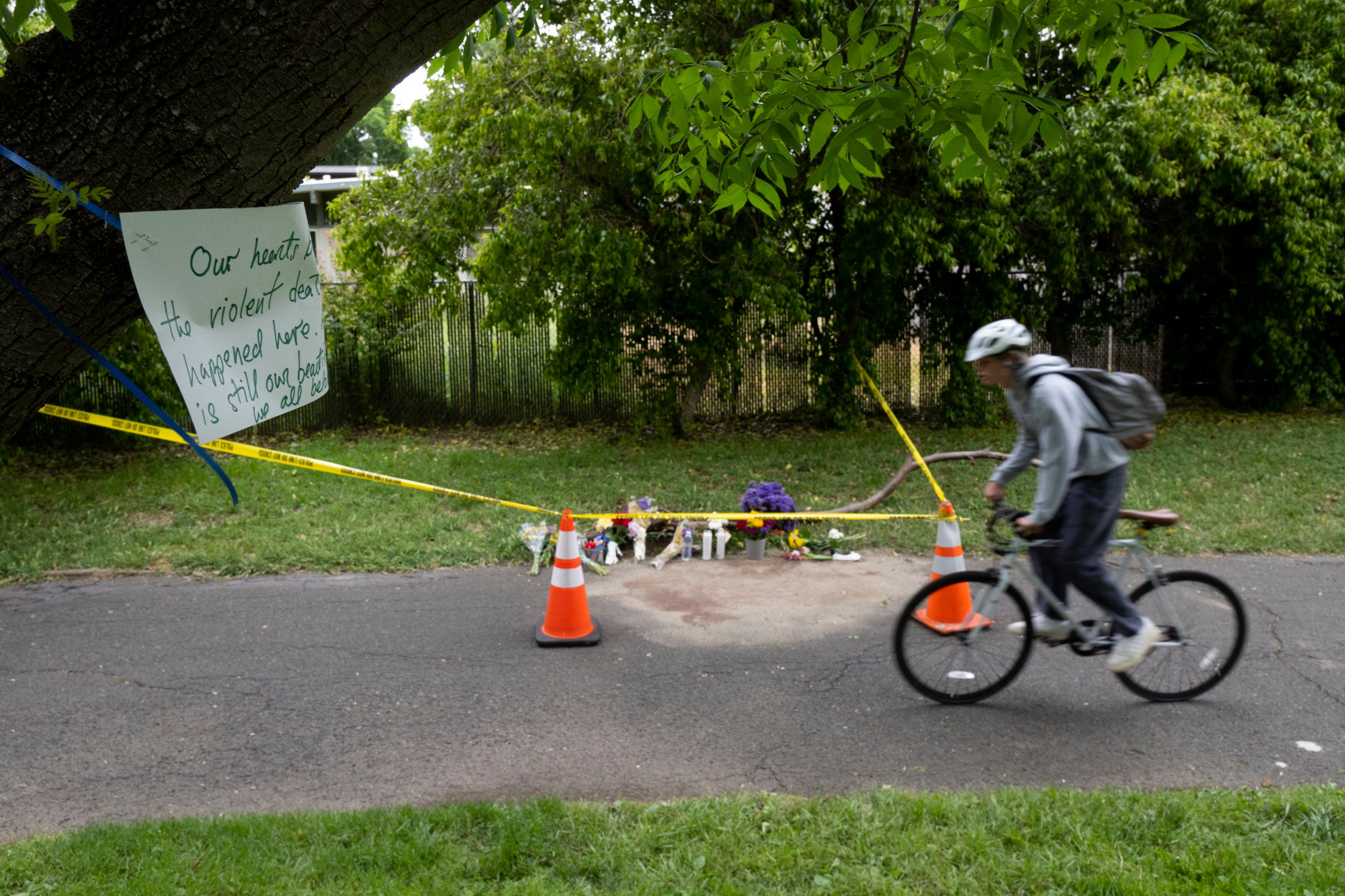 A cyclist rides past a memorial of flowers marking the location that Karim Abou Najm, a graduating senior at UC Davis, was fatally stabbed in Sycamore Park in Davis