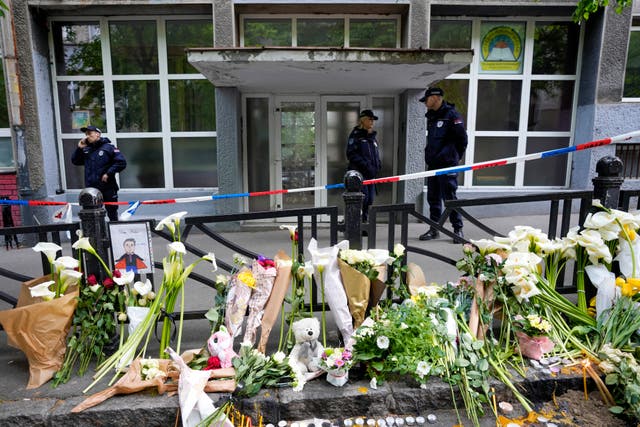 <p>Police officers guard the Vladimir Ribnikar school in Belgrade – behind tributes to those killed </p>