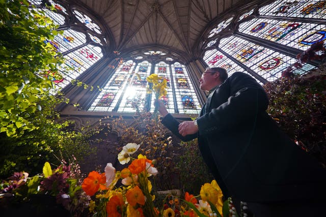 <p>Florist Shane Connolly, who will be arranging the flowers within Westminster Abbey, holding a bunch of poppies among the coronation service flowers, at Chapter House, Westminster Abbey (Yui Mok/PA)</p>