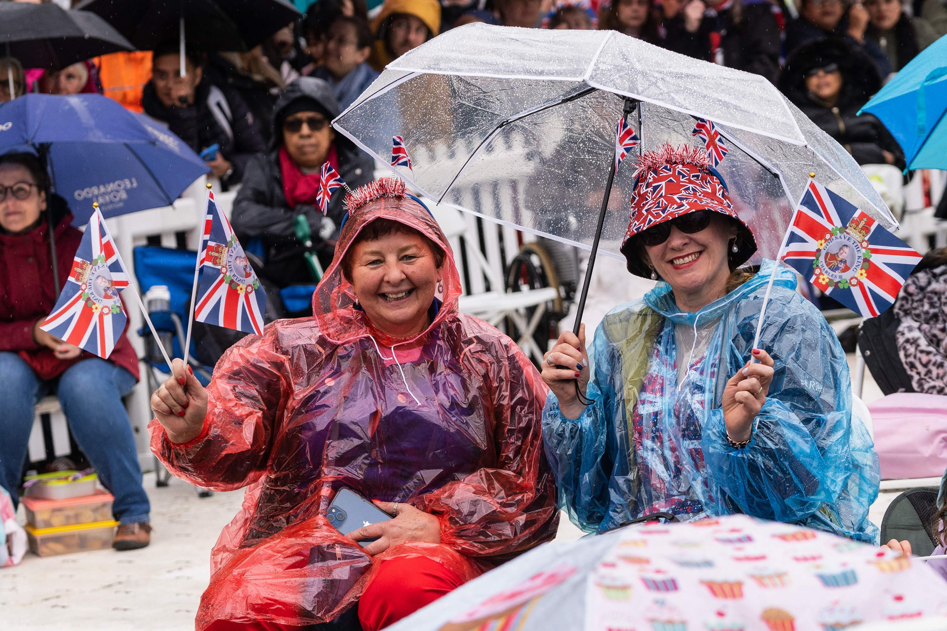 Well-wishers protect themselves against the rain as they wait along the route of the 'King's Procession'
