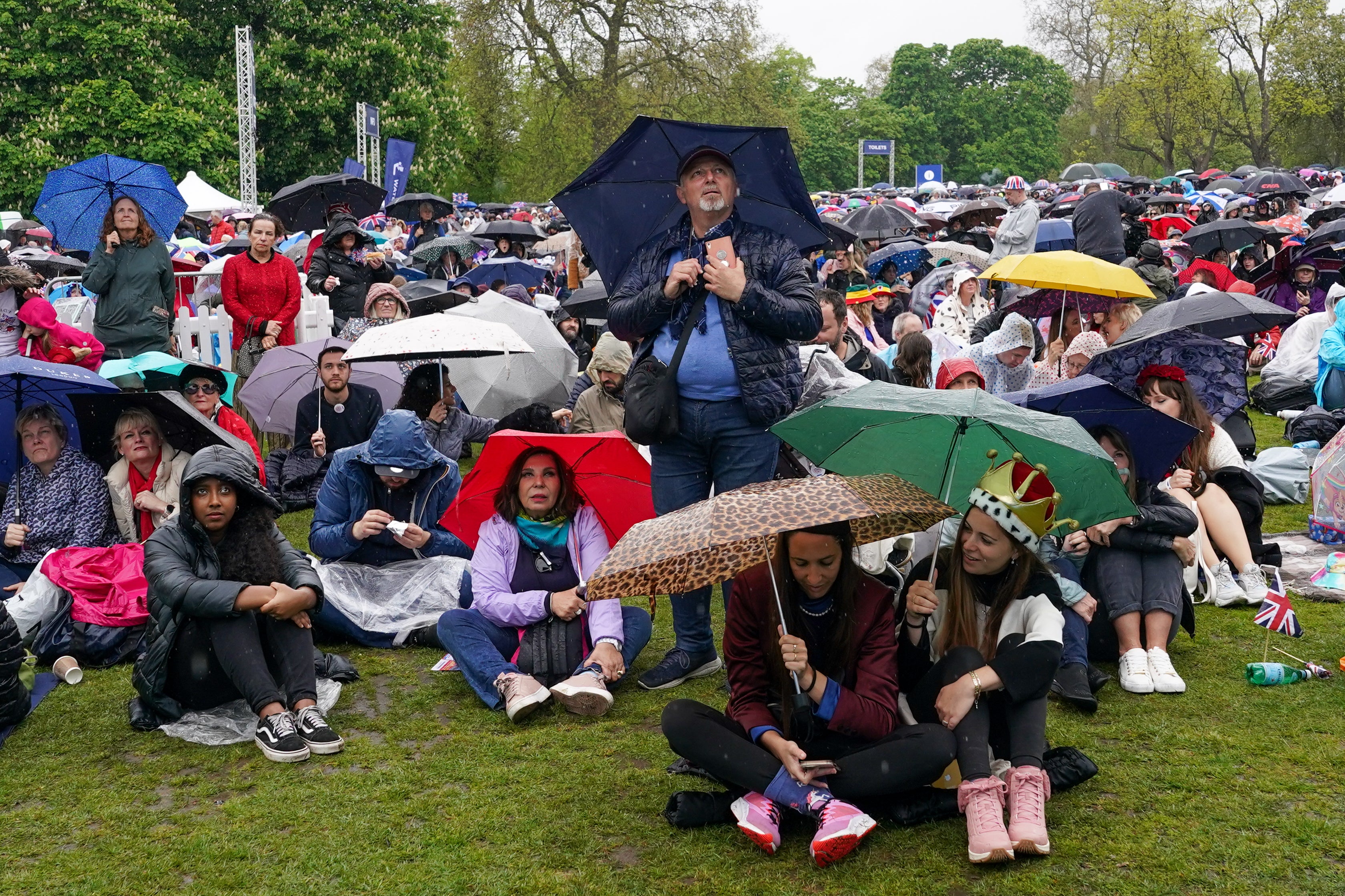 Rain soaked members of the public in Hyde Park watch giant screens showing coverage of the Coronation