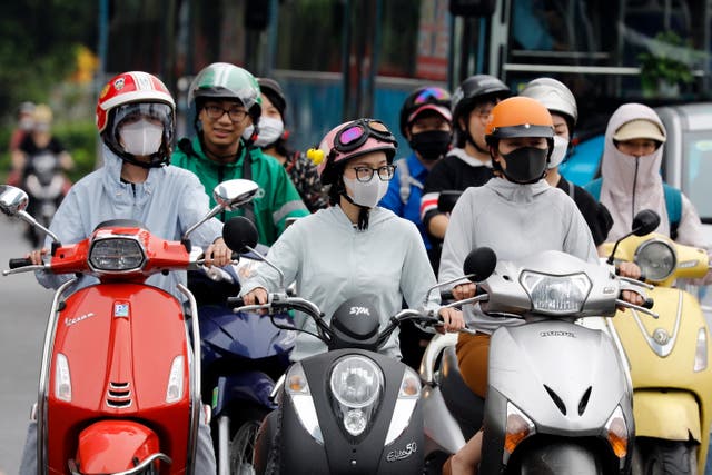 <p>People wear long clothing to protect themselves from the heat while riding motorcycles along a street in Hanoi on 8 May</p>