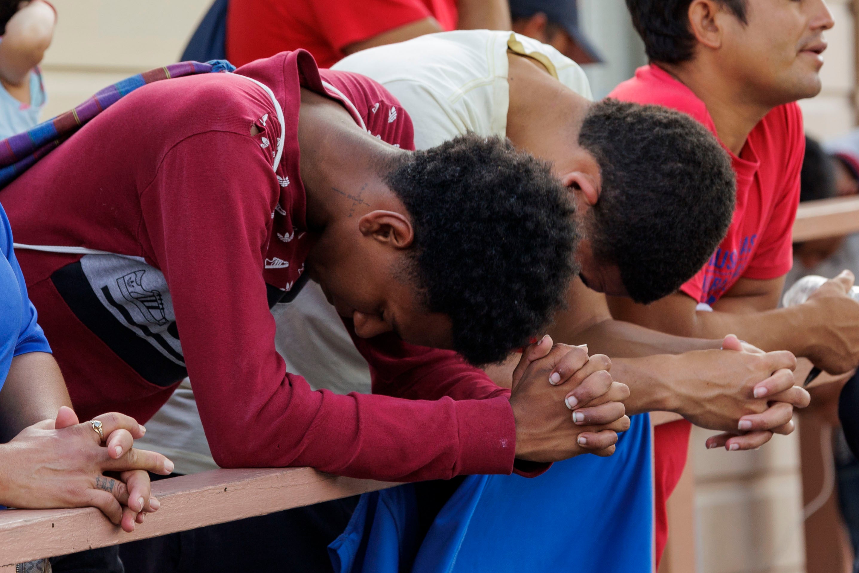 pTwo migrants bow their heads during a prayer at a vigil at the Ozanam Center, a homeless and migrant shelter, on 8 May 2023 in Brownsville, Texas/p