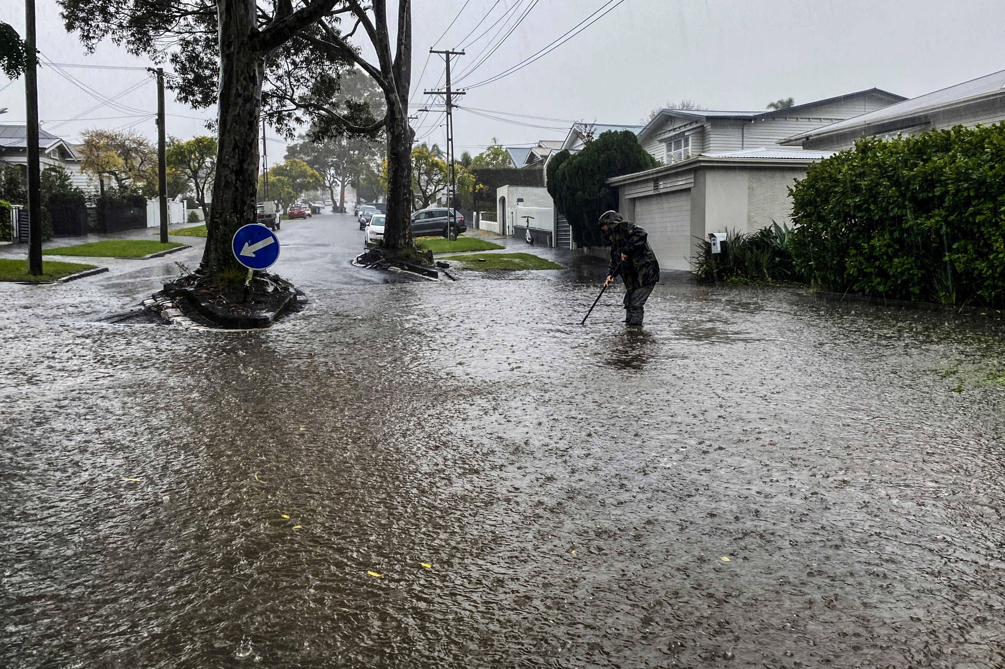 A man attempts to clear a drain in a flooded street in central Auckland, New Zealand