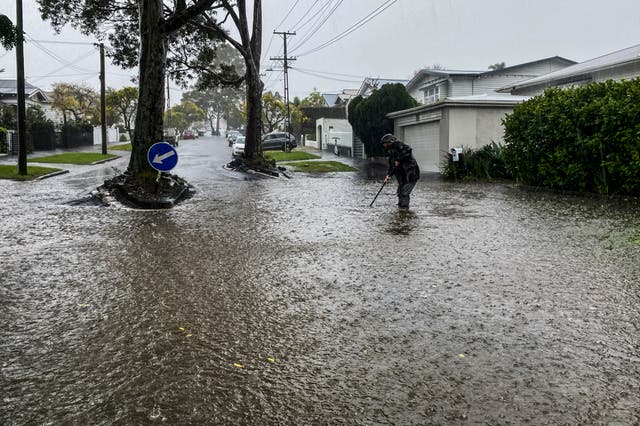 <p>A man attempts to clear a drain in a flooded street in central Auckland, New Zealand</p>