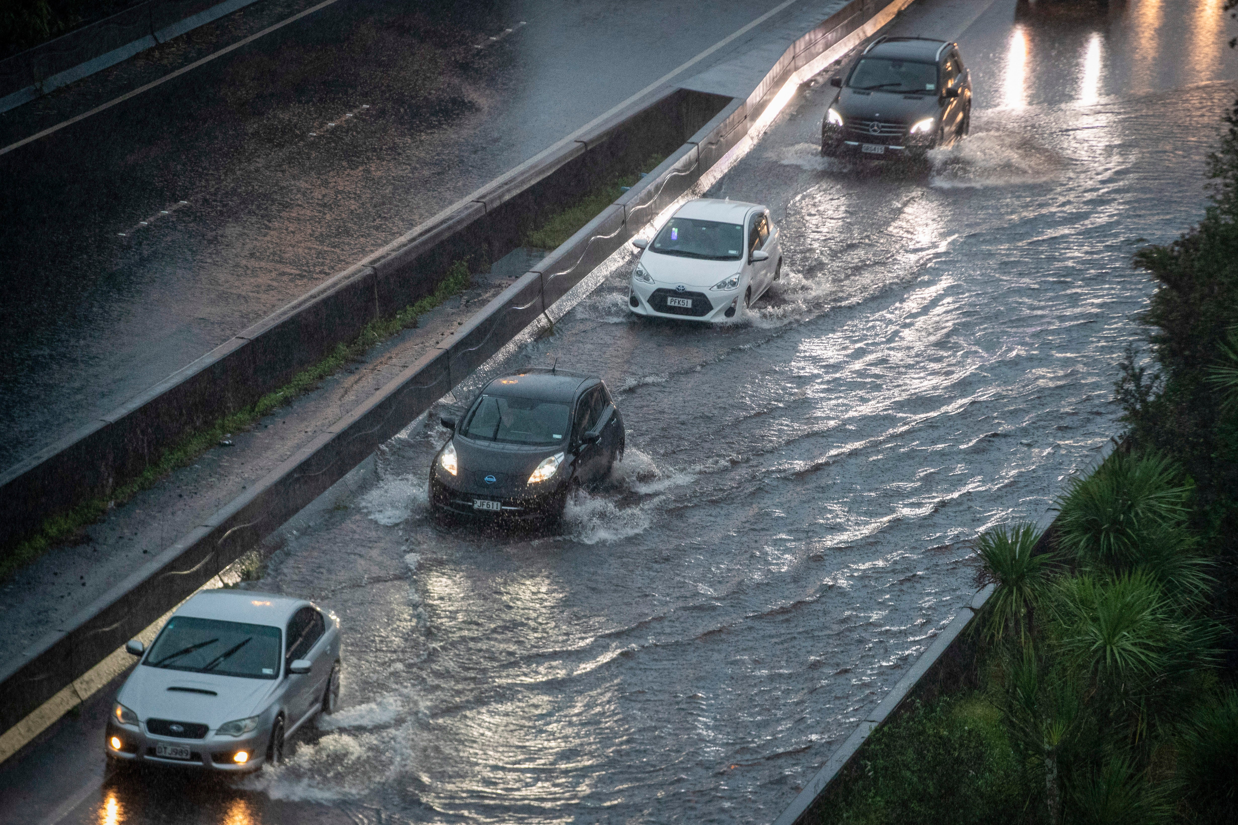 Cars move through water in the flooded streets of a motorway in central Auckland