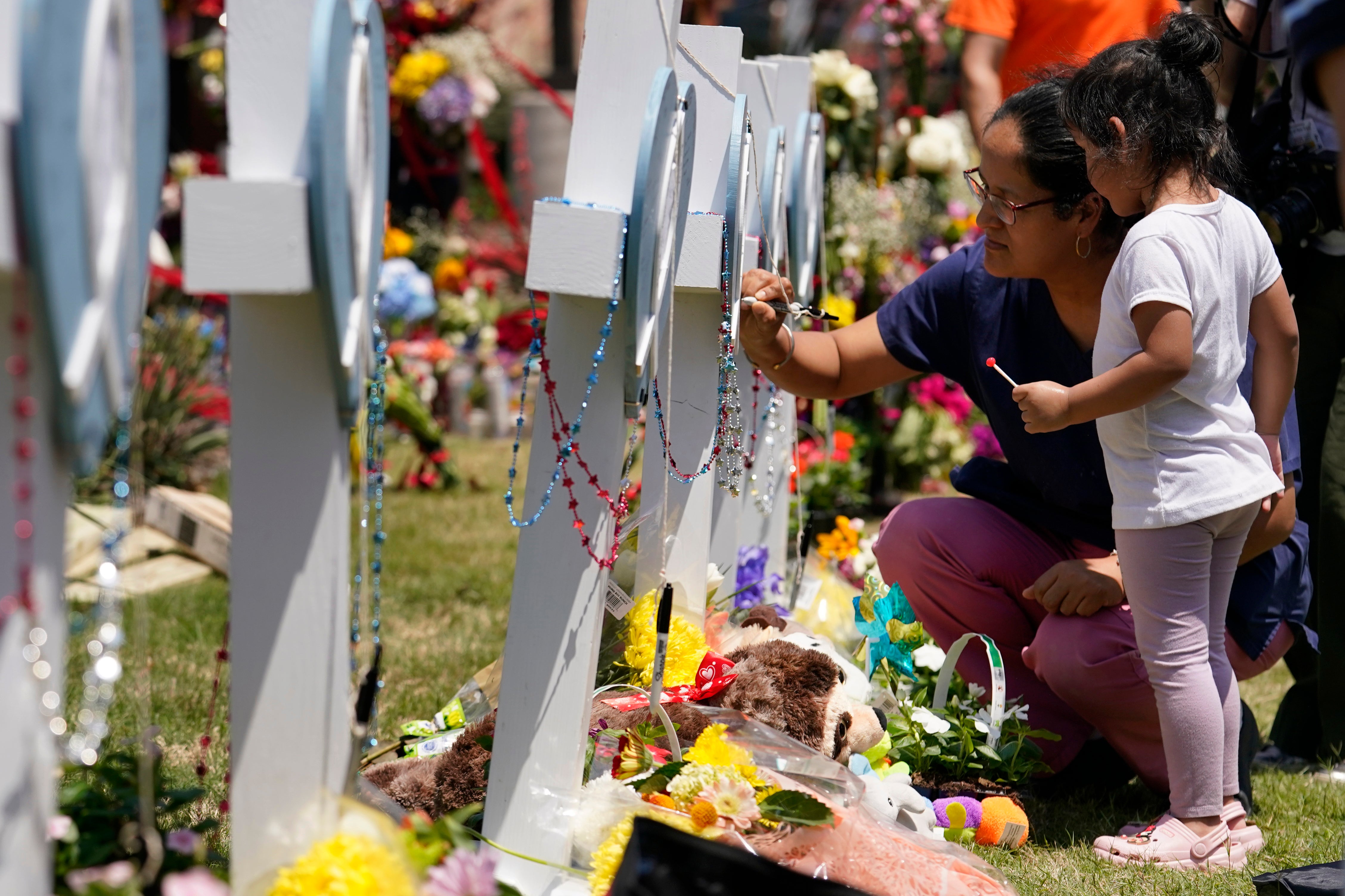 A woman signs a cross as a child looks on at a makeshift memorial by the mall where several people were killed in Saturday's mass shooting, Monday, May 8, 2023, in Allen, Texas