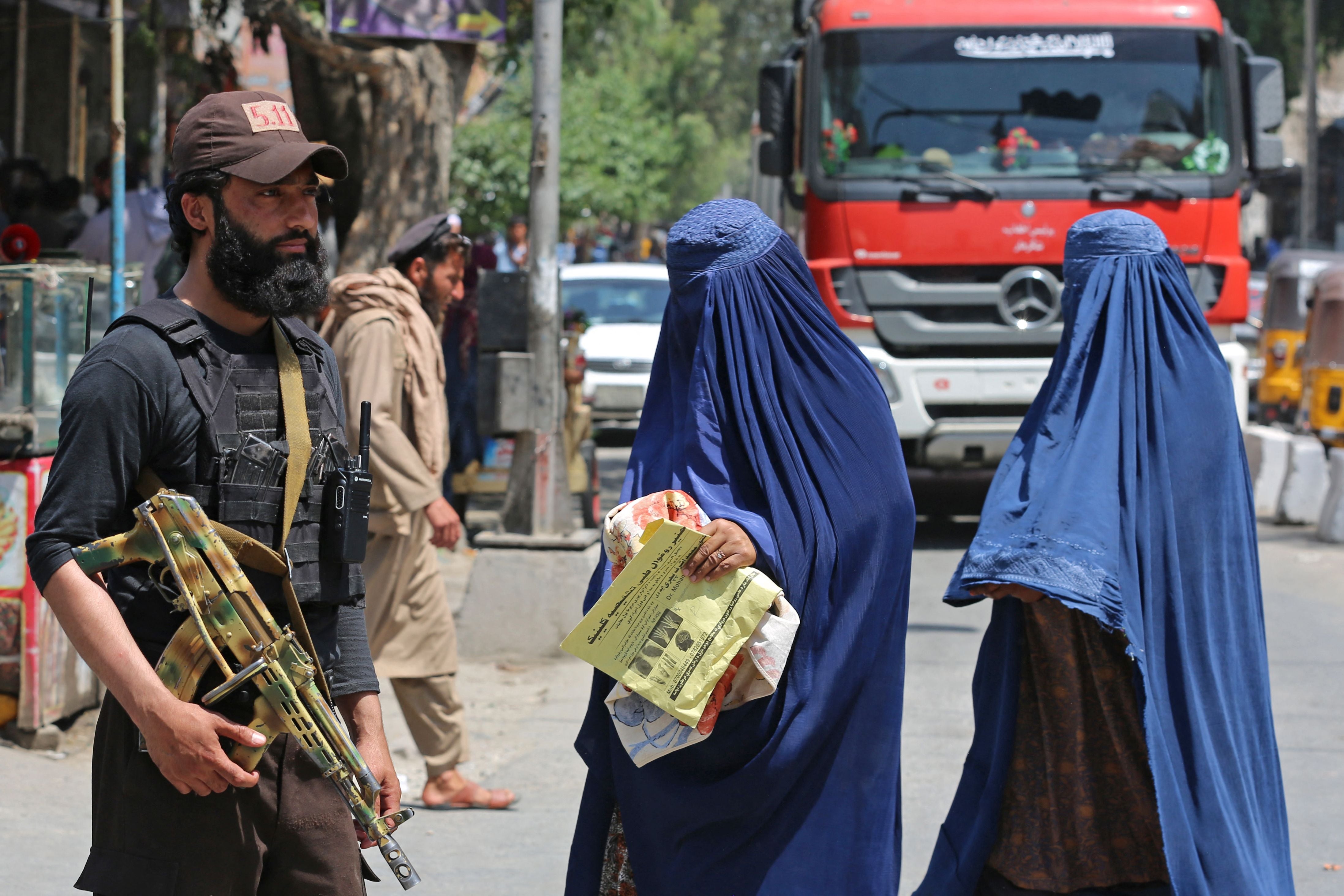 Afghan burqa-clad women walk past a Taliban security personnel along a street in Jalalabad