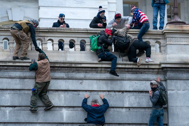 <p>Rioters climb a wall of the US Capitol on January 6 </p>
