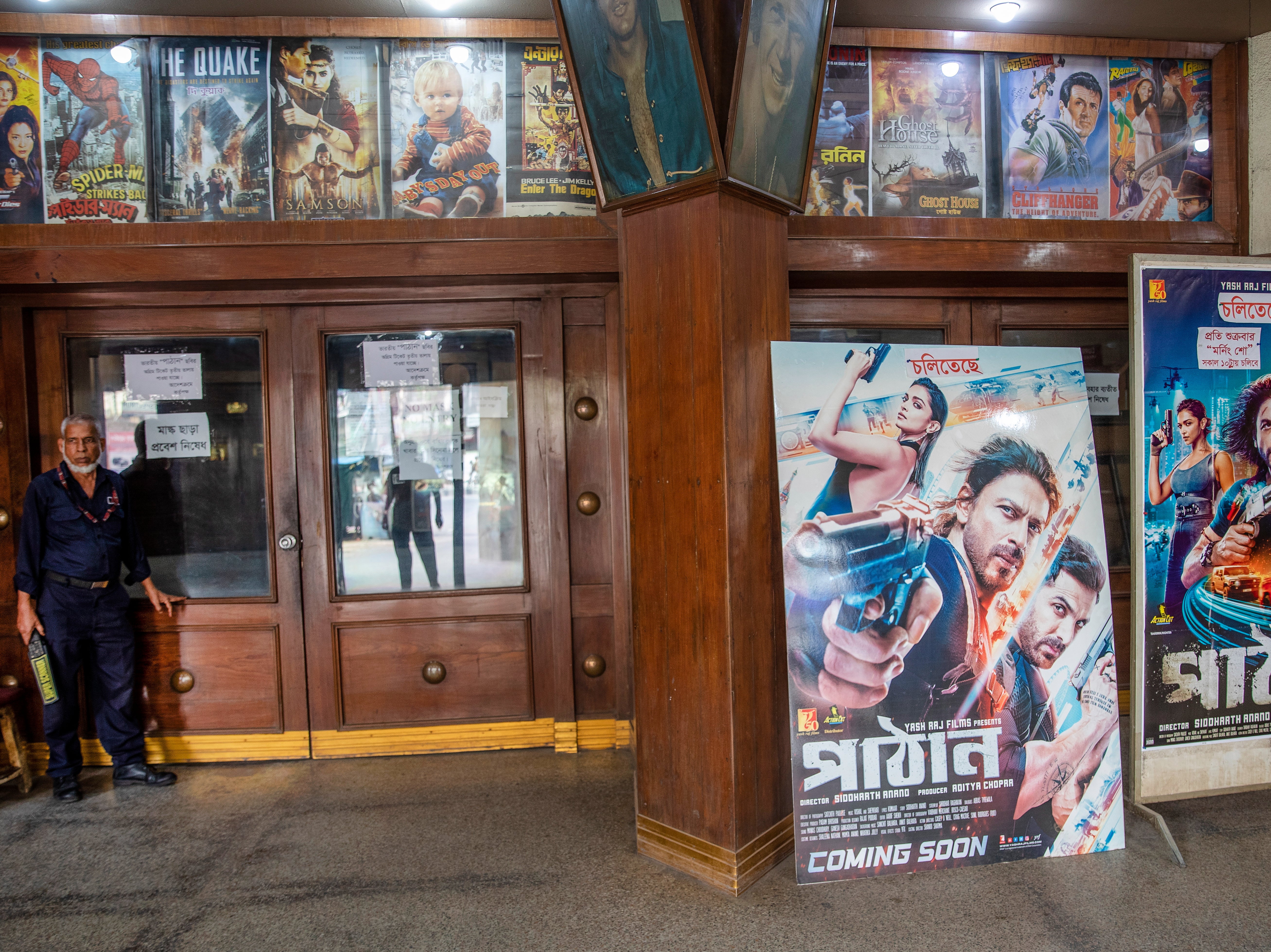 A Bangladeshi security guard stands next to posters of the Indian Hindi-language movie 'Pathaan'