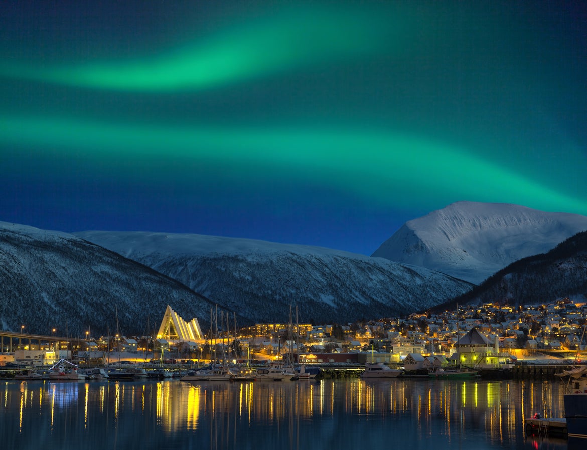 <p>A view of an illuminated Tromso with the Northern Lights over the city </p>