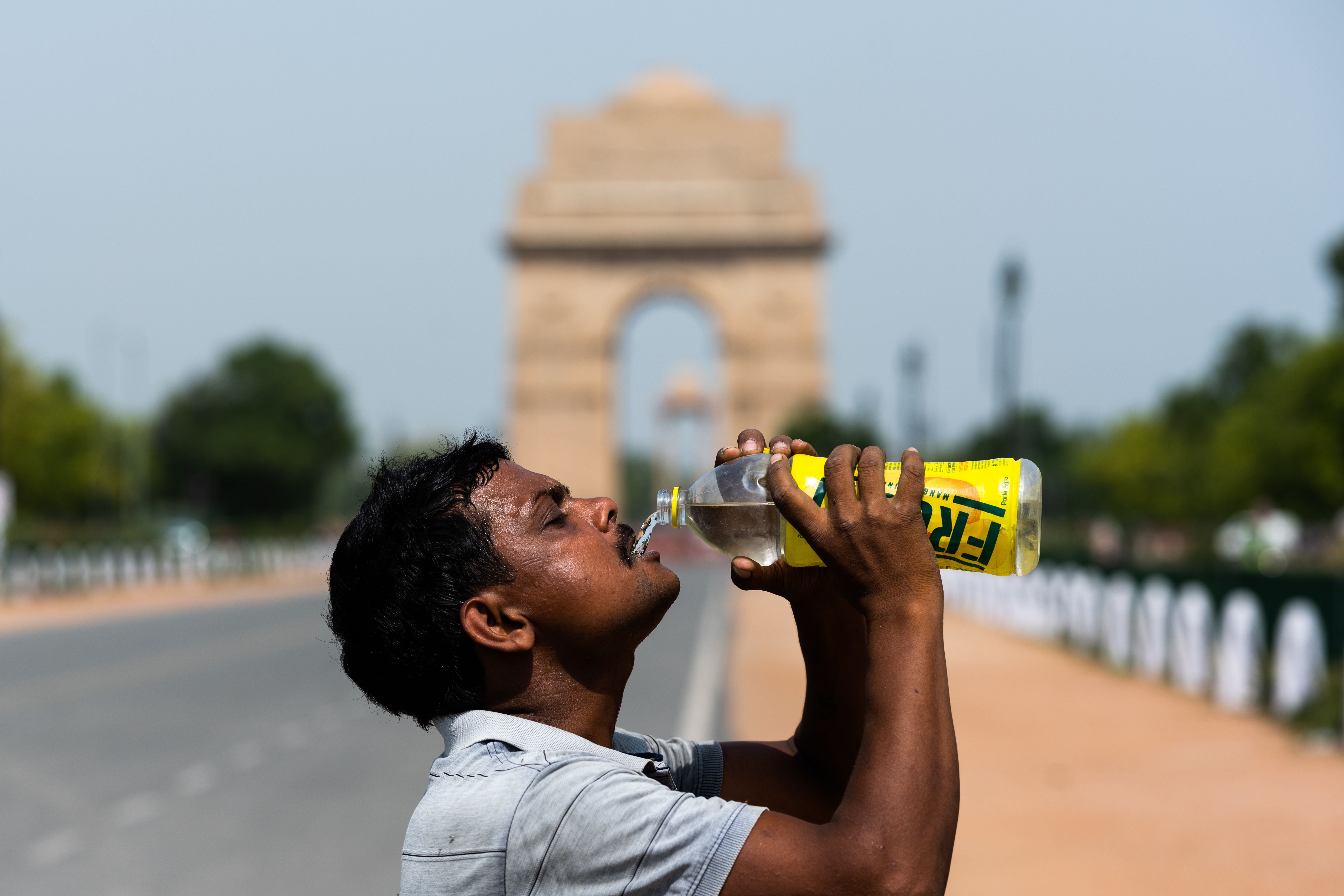 A worker quenches his thirst with water from a bottle taking a break from cleaning weeds from a park near India Gate amid rising temperatures in Delhi
