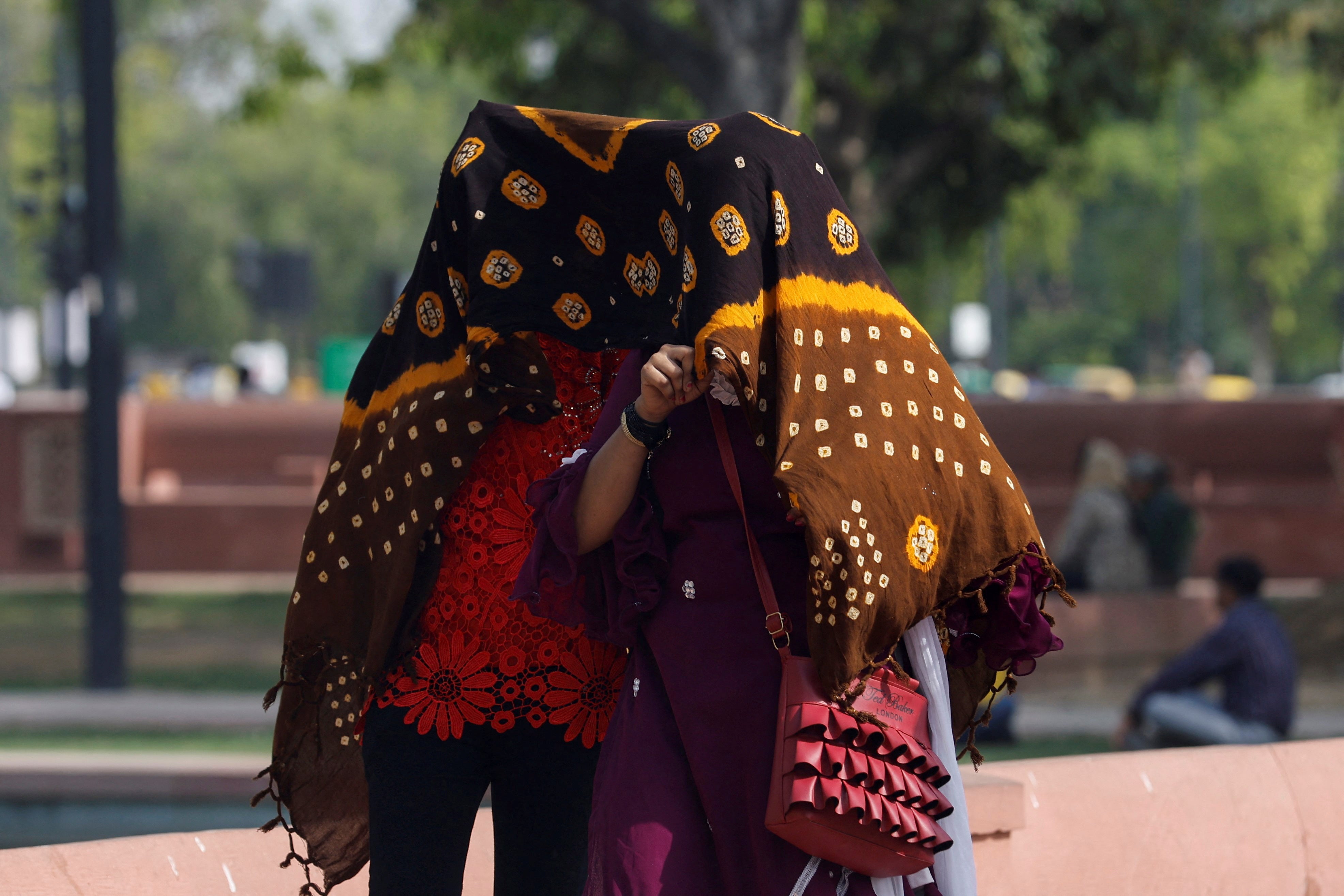 Women take shelter under a cloth, as they walk across a garden on a hot summer day near India Gate