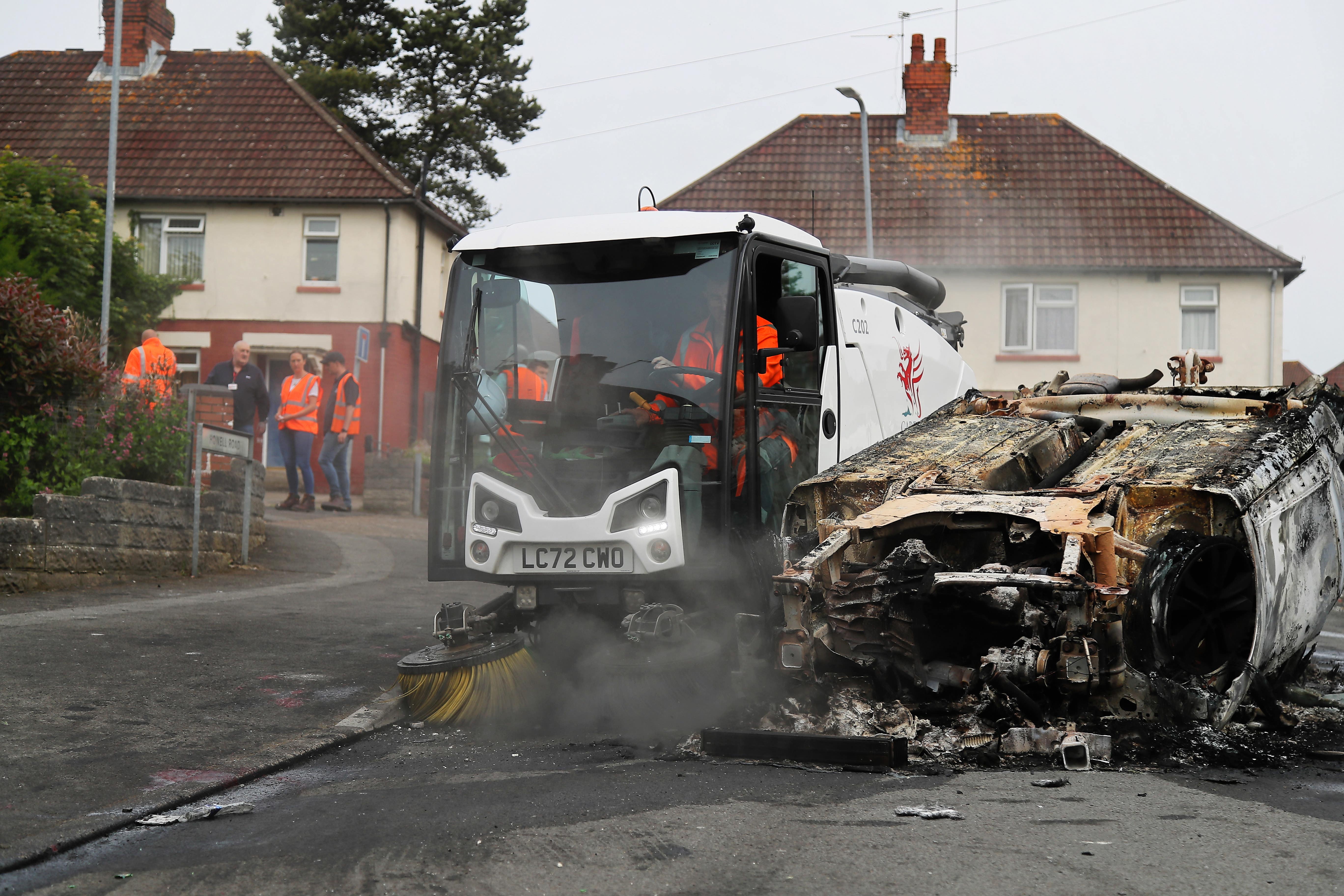 Council workers clear debris from the area immediately around a car that was set alight in Ely, Cardiff, following the riot that broke out after two teenagers died in a crash (PA)