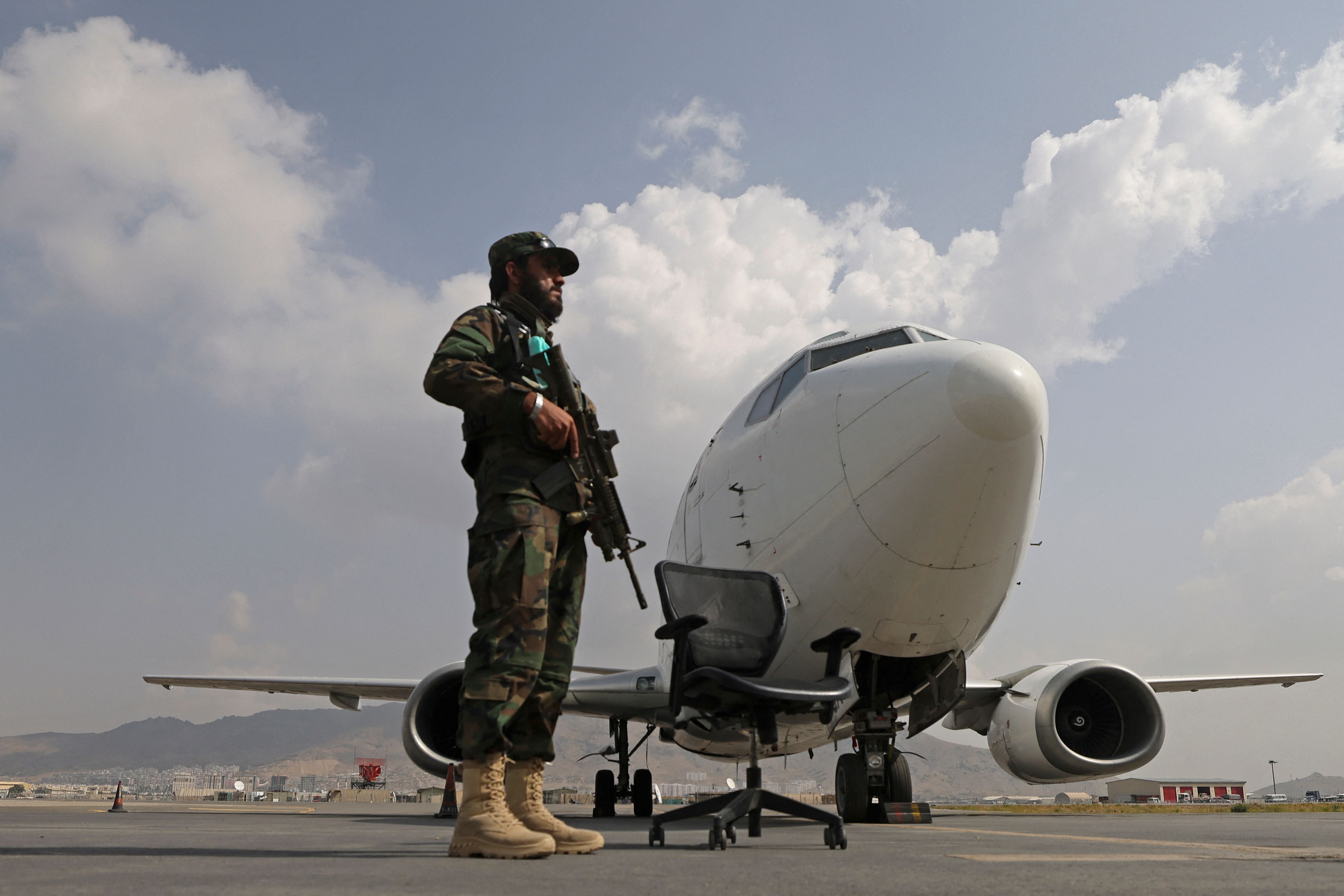 A Taliban fighter stands guard next to an Ariana Afghan Airlines aircraft on the tarmac at the airport in Kabul
