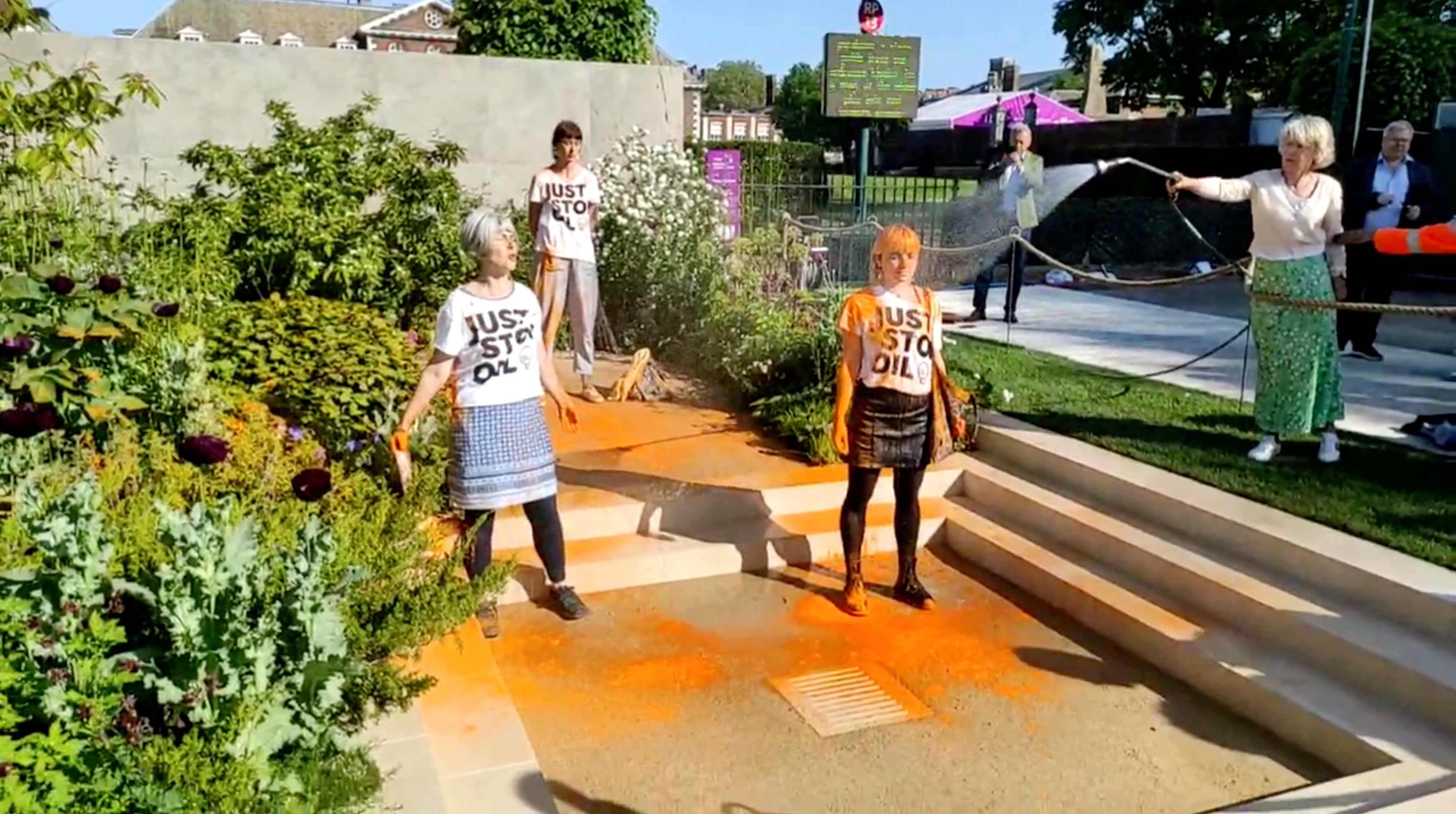 A woman douses Just Stop Oil protesters with water after they throw orange paint over a Chelsea Flower Show exhibit in London