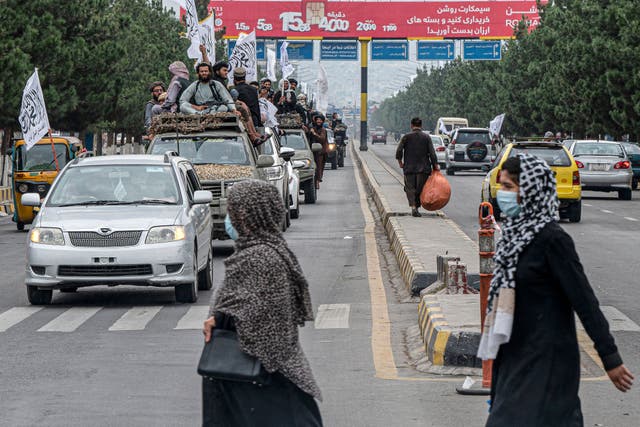 <p>Afghan women cross a road as Taliban fighters ride in a convoy to celebrate their victory day near the US embassy in Kabul</p>